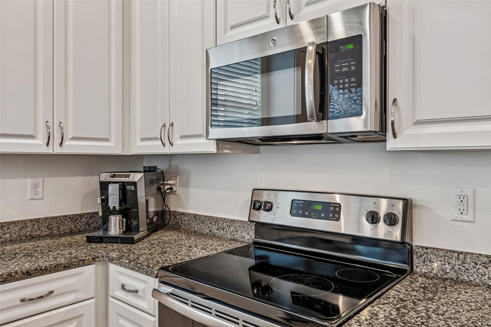 Modern stainless steel range and microwave are set within a smartly arranged workspace, flanked by generous cabinet storage.