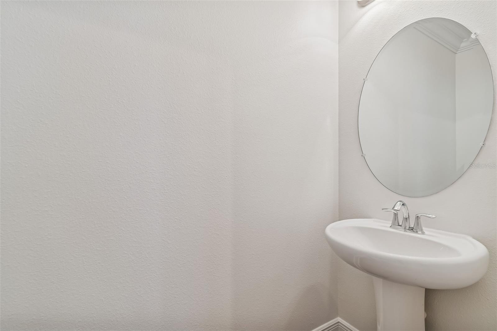 Simple and bright powder room with pedestal sink, round mirror, and soft neutral tones for a clean, fresh look.