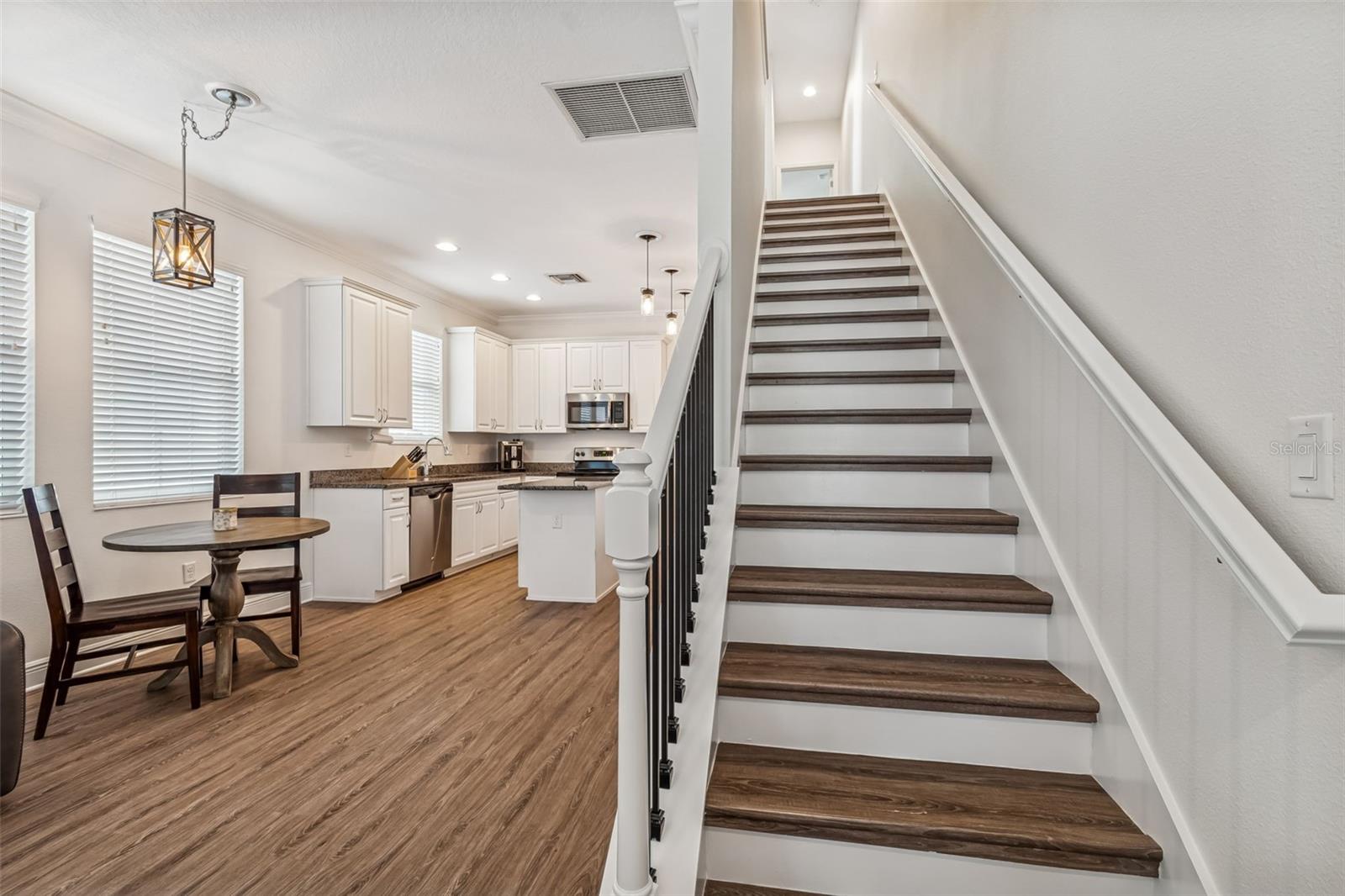 Stylish staircase with dark wood treads and white risers leads to the second floor, set beside the open kitchen and dining area.