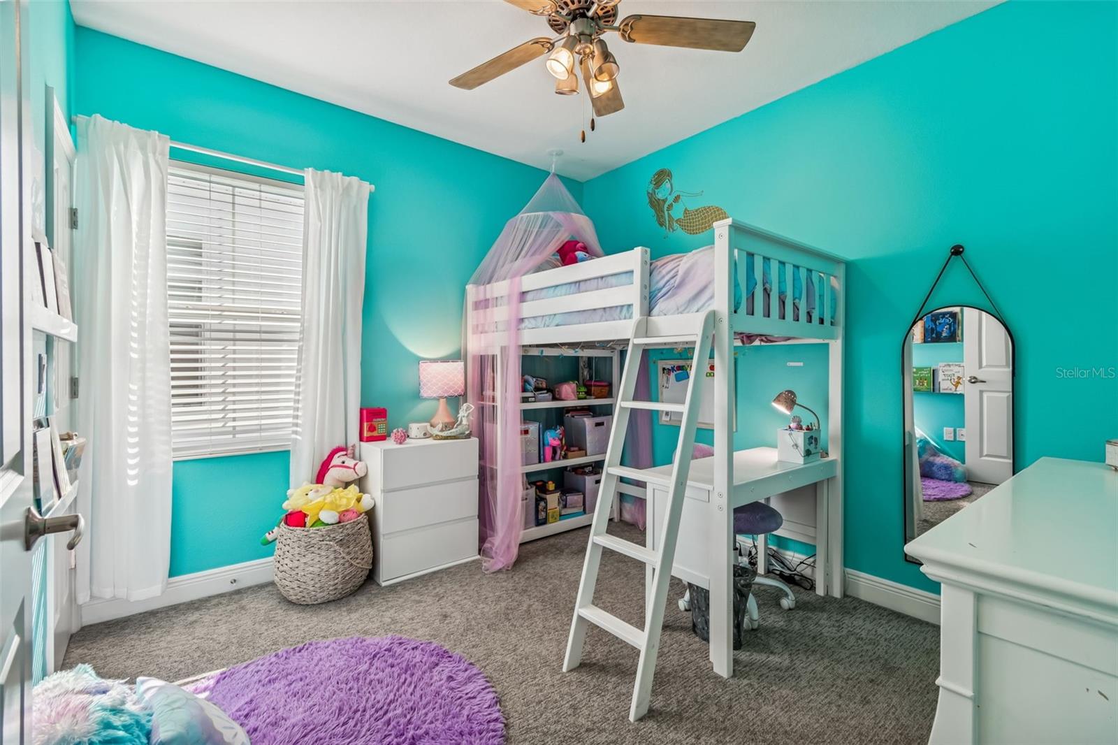 Cheerful bedroom filled with natural light, featuring fun teal walls, ceiling fan, and a multifunctional loft bed with integrated desk and storage.