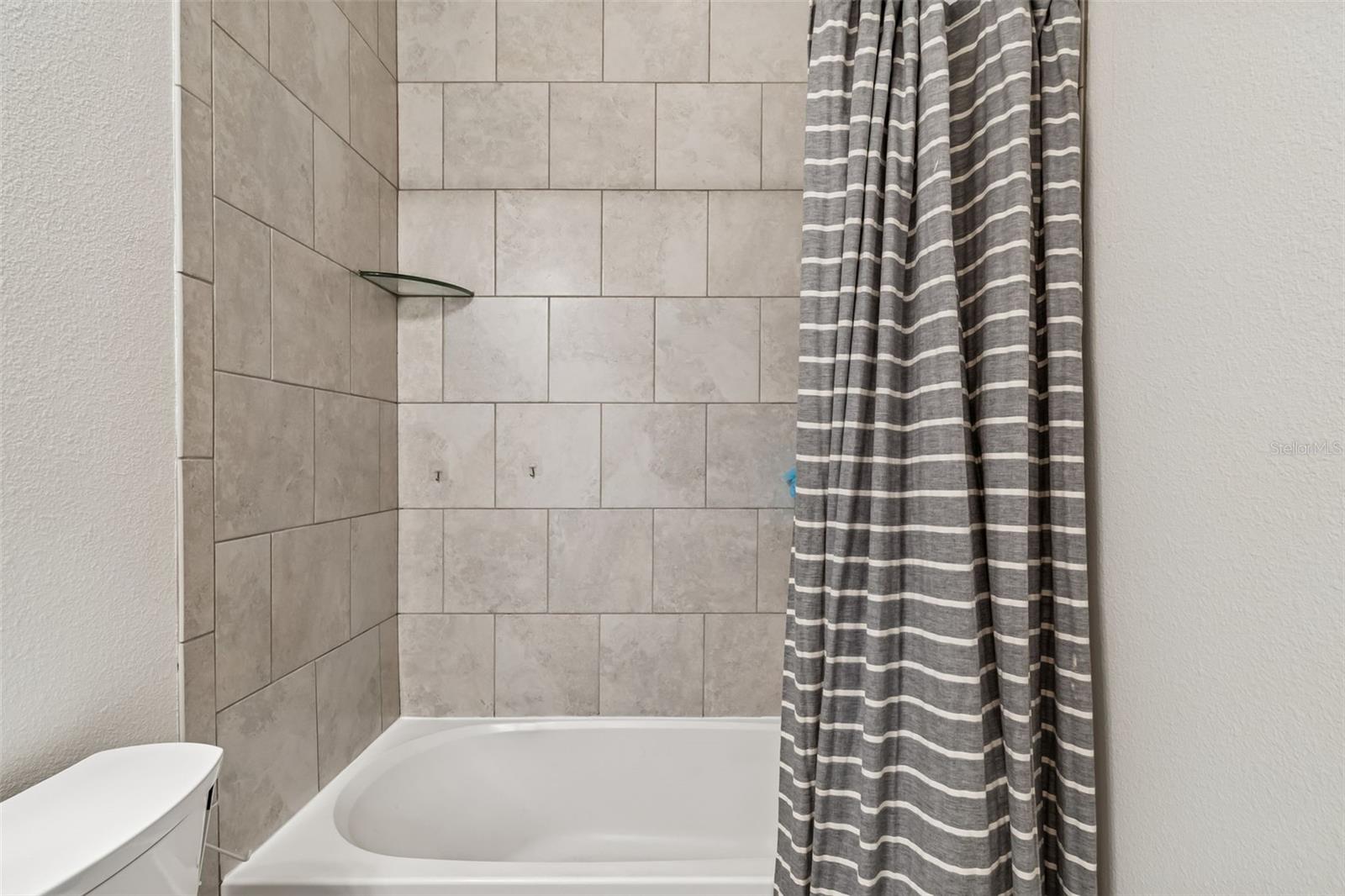 Neutral-toned tile surrounds the tub in this clean and modern full bath, with built-in corner shelf for added convenience.