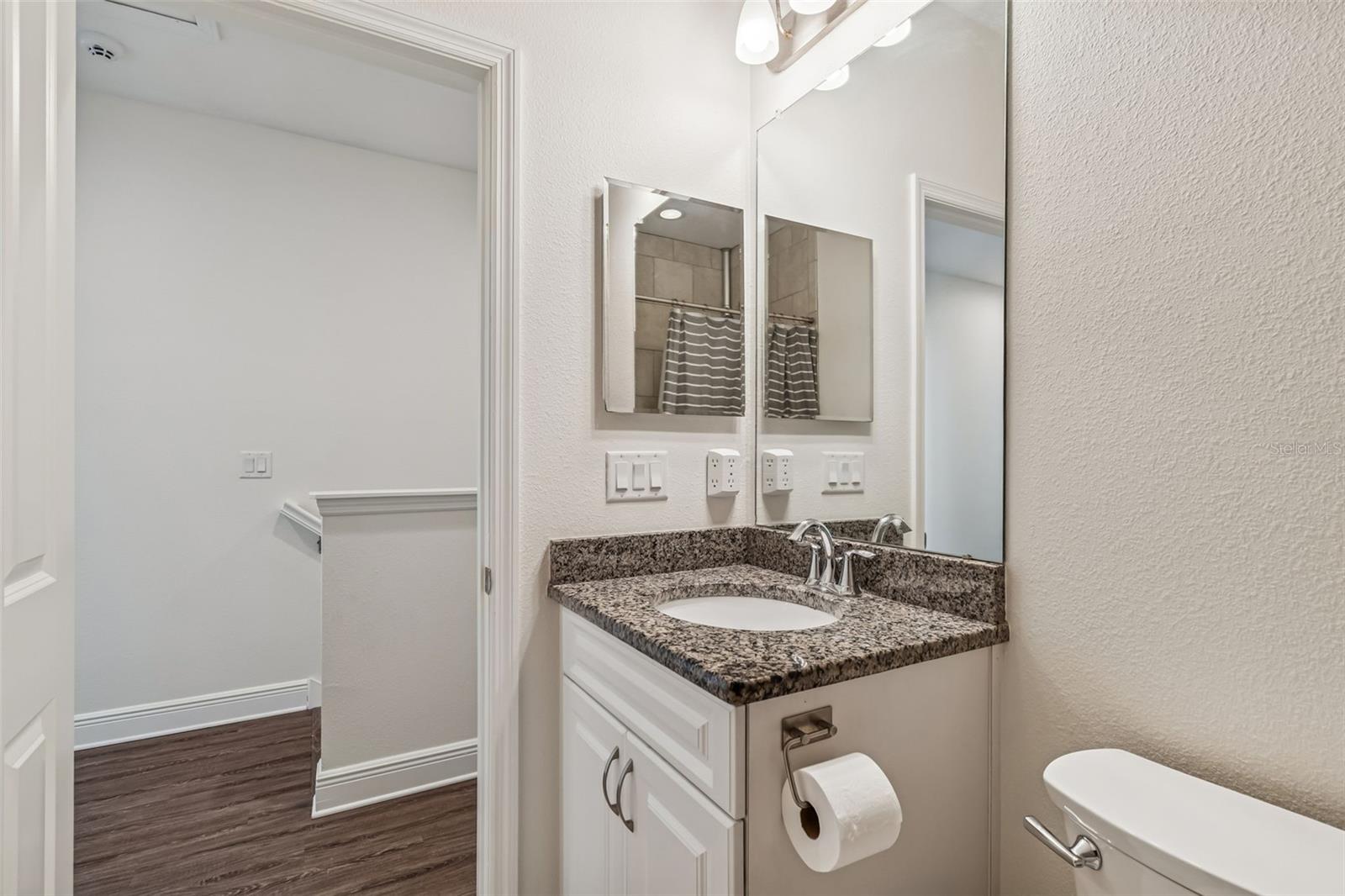 Conveniently located near the bedrooms, this full bath features a granite vanity, sleek mirror, and neutral tile details.