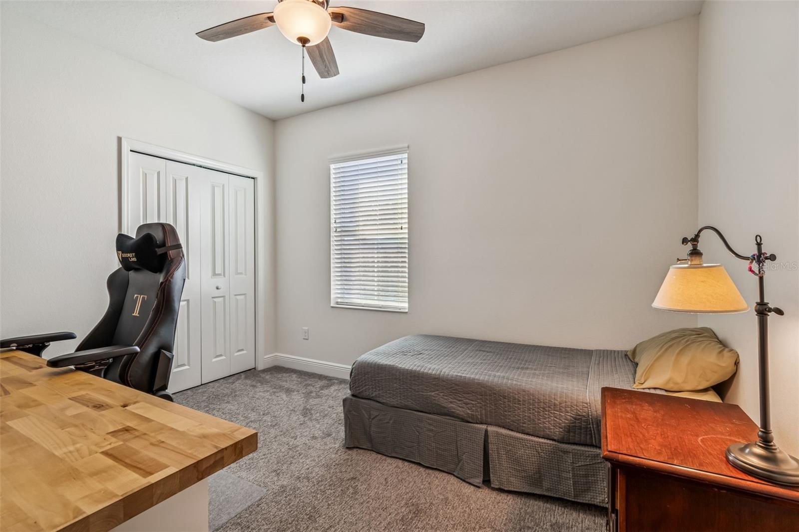 Bright and functional guest or teen room with plush carpeting, window blinds, and ceiling fan for comfort.