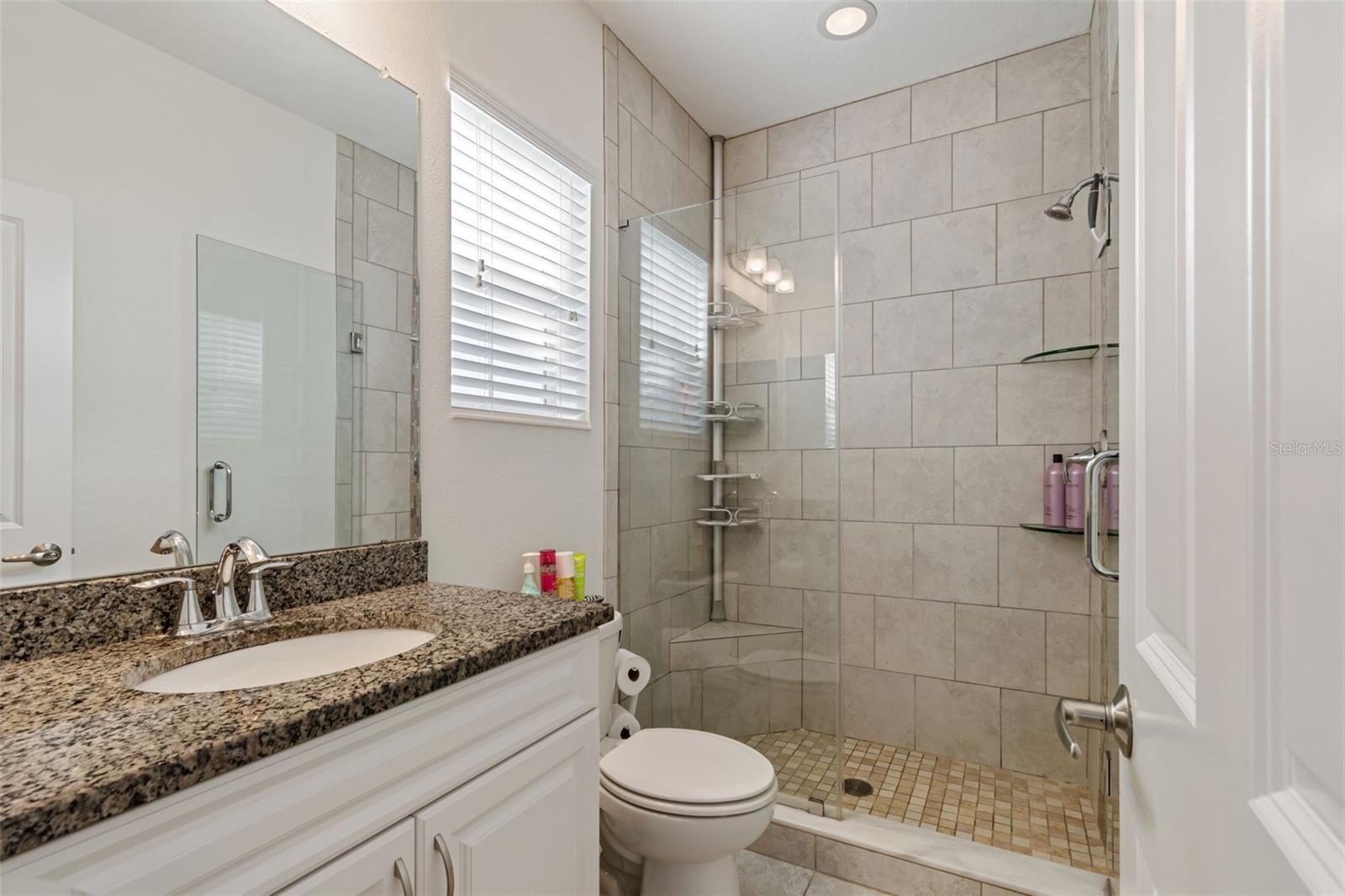Clean and modern, with a spacious walk-in shower and extended granite counter providing ample space.