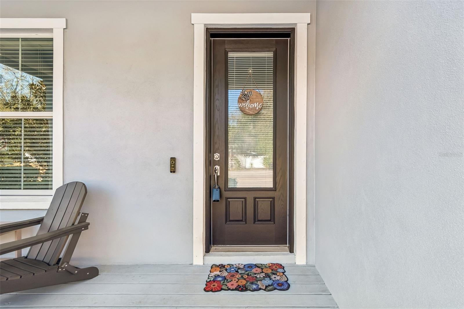 Dark-stained glass-inset door offers privacy while allowing natural light to filter in; accented with a cheerful welcome sign.