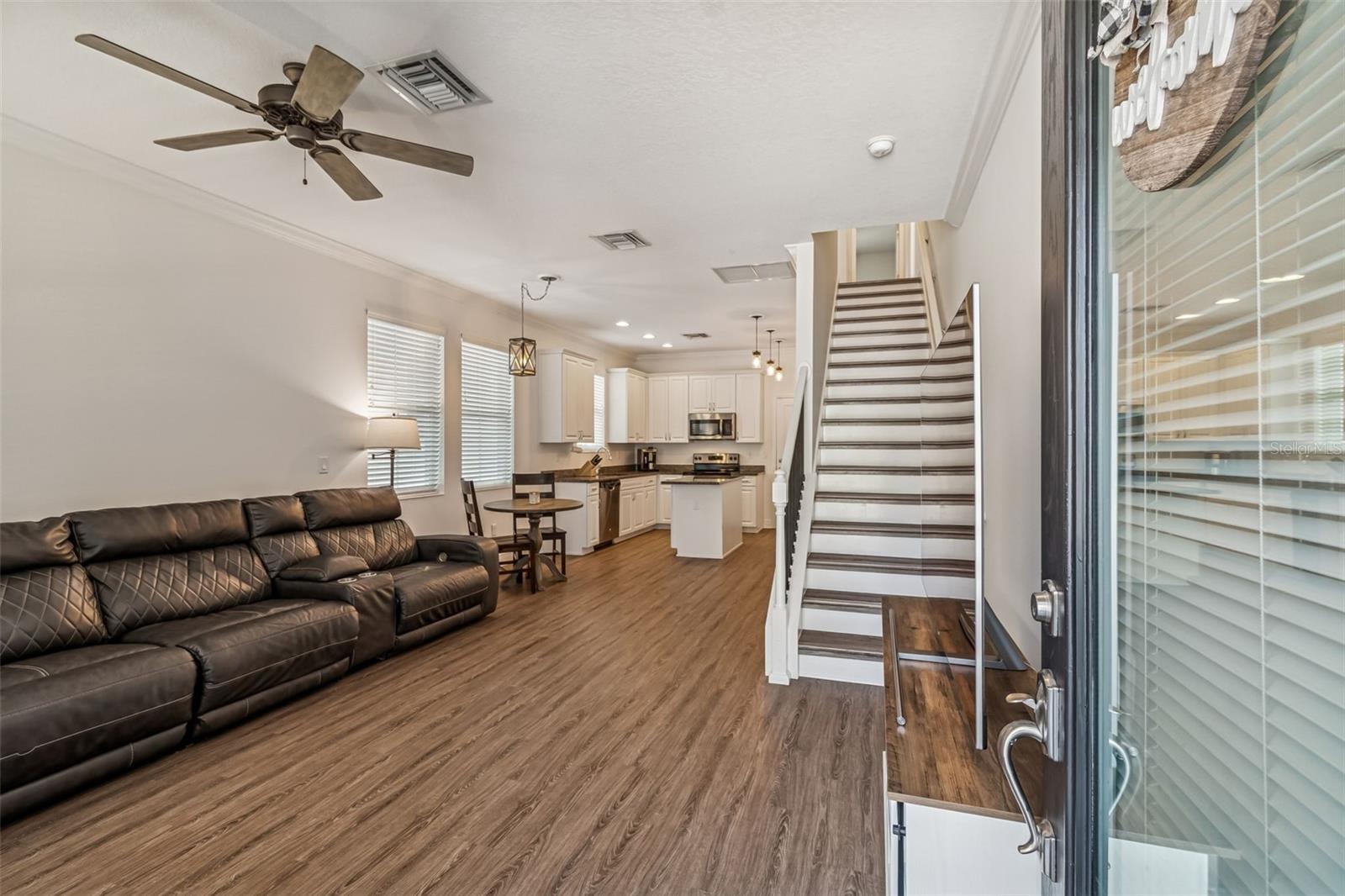Open-concept layout featuring rich wood-style flooring, neutral walls, and direct sightlines to the kitchen and staircase.