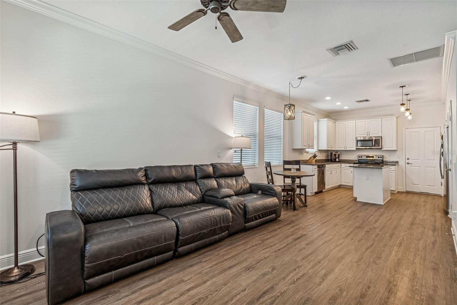 Spacious living area with recessed lighting, ceiling fan, and natural light pouring in from multiple windows; flows seamlessly into the eat-in kitchen.