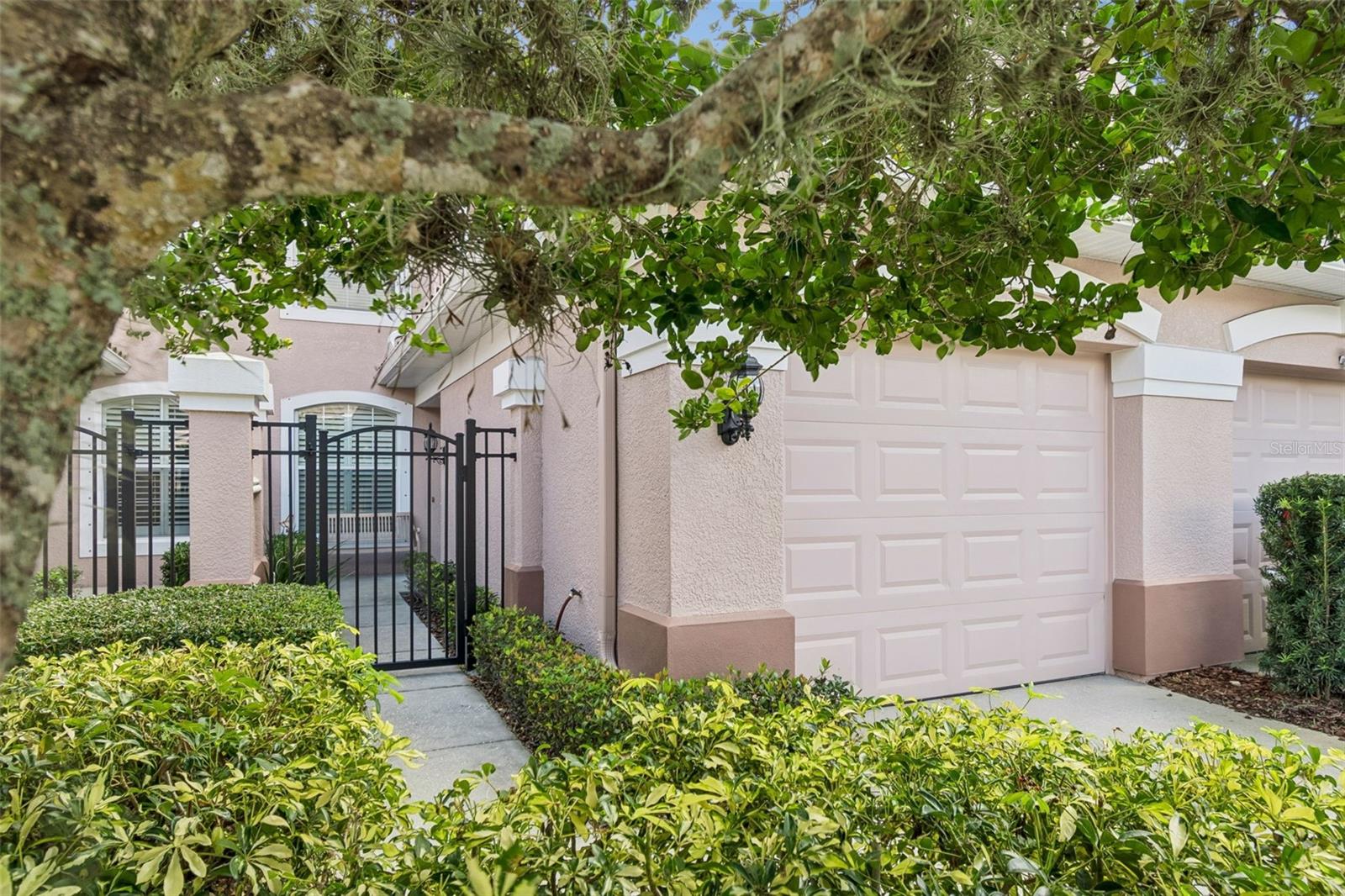 The approach to the home is framed by privacy fencing, lush landscaping, and direct gated access to the courtyard.