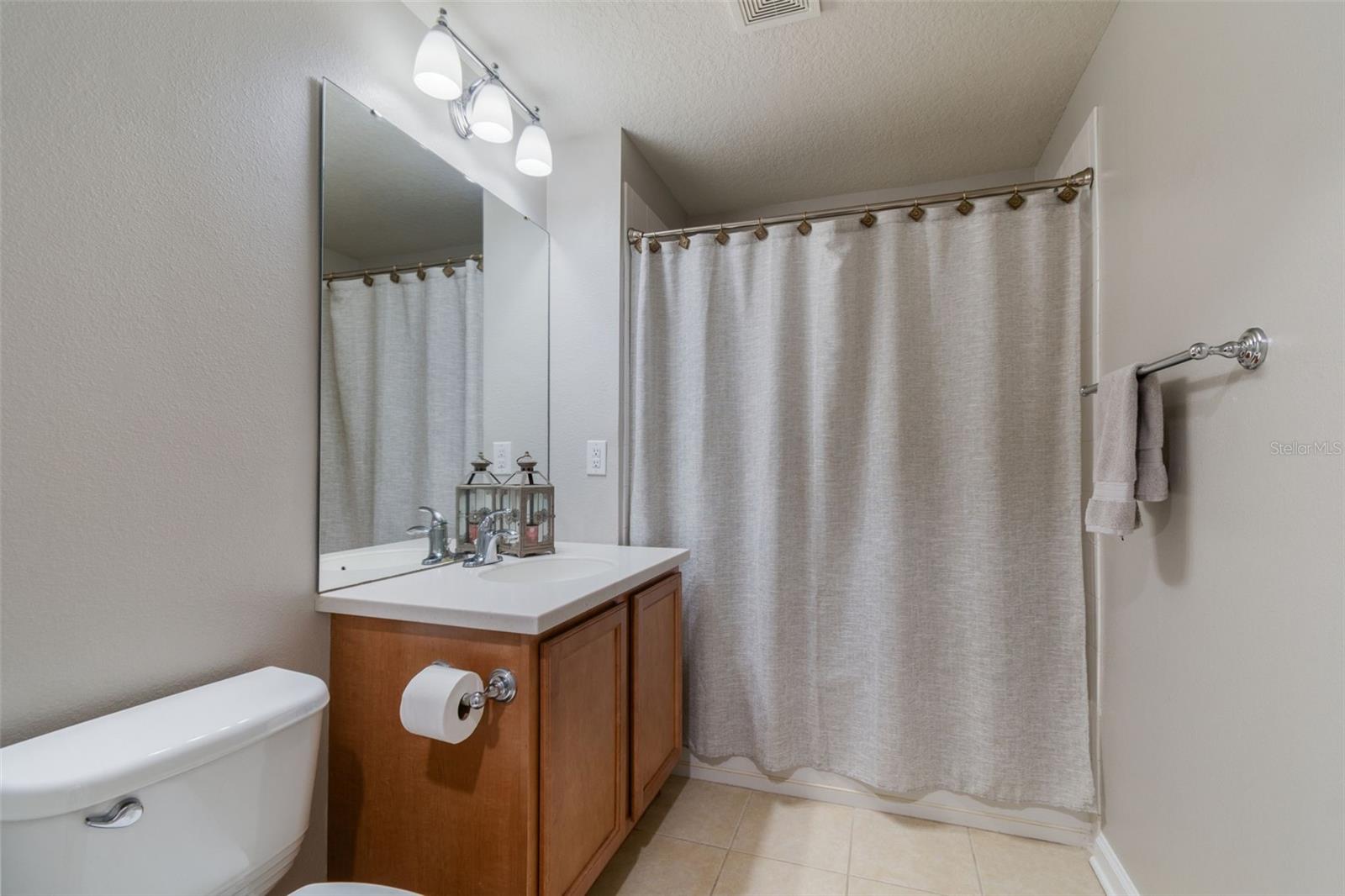 A clean and classic full bath with single vanity, modern lighting, and a shower/tub combo behind a neutral curtain.