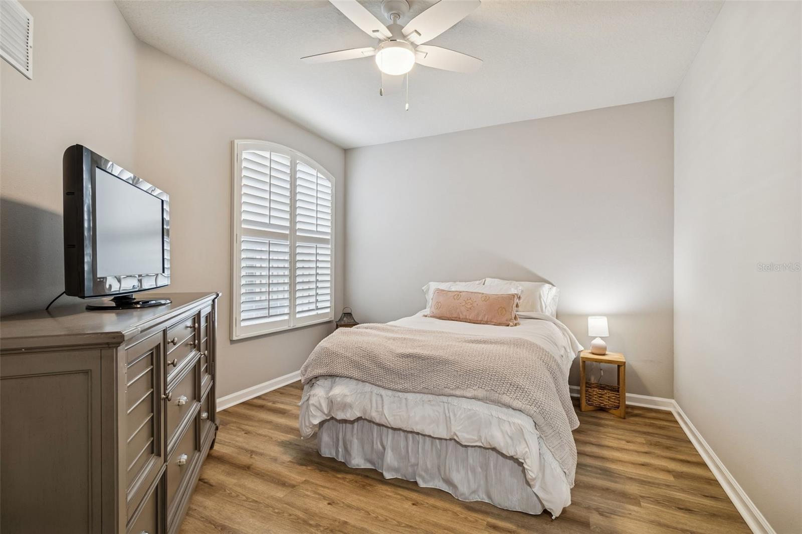 Featuring soft paint tones, wood-look flooring, and an arched window with plantation shutters for added privacy and light.