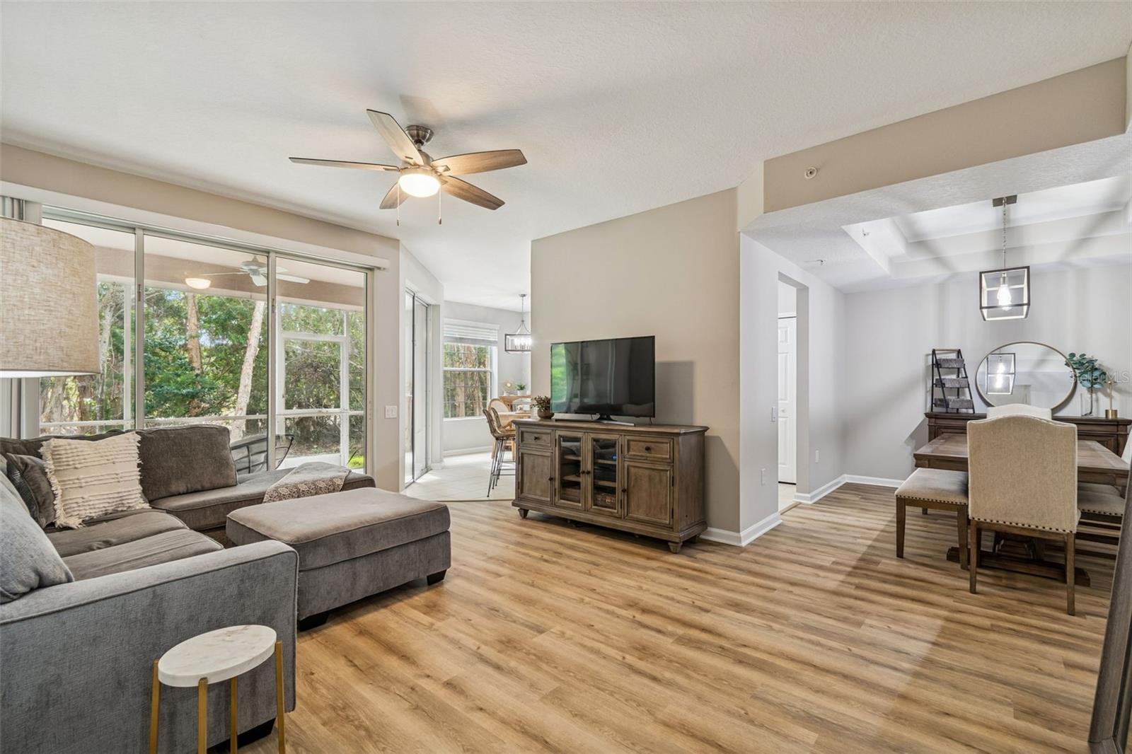 Open-concept living room with wood-look floors, large sectional, and stunning views through oversized sliding glass doors to the screened patio and nature beyond.