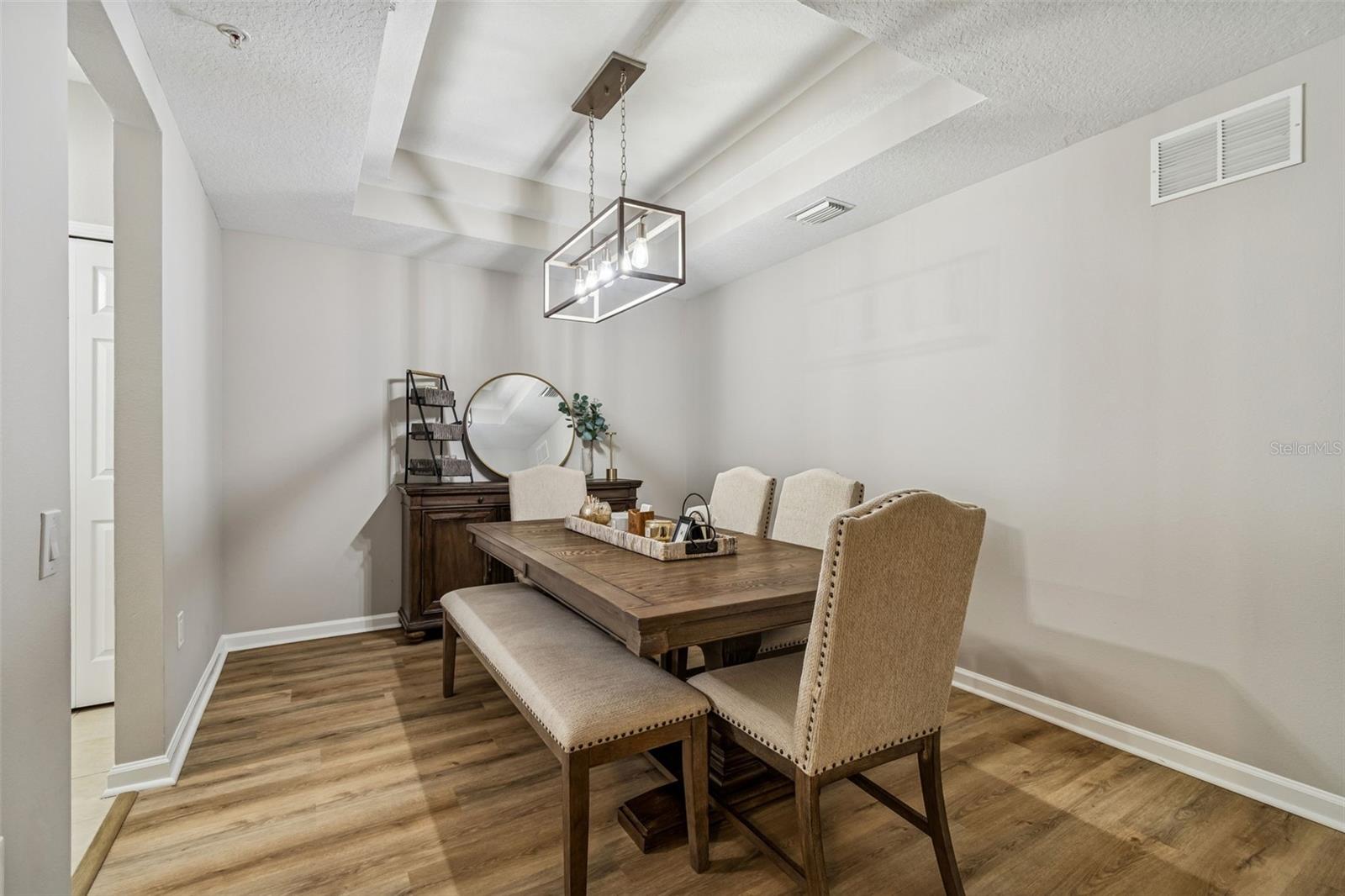Elegant formal dining room with tray ceiling and a rectangular chandelier over a wood farmhouse-style dining set.