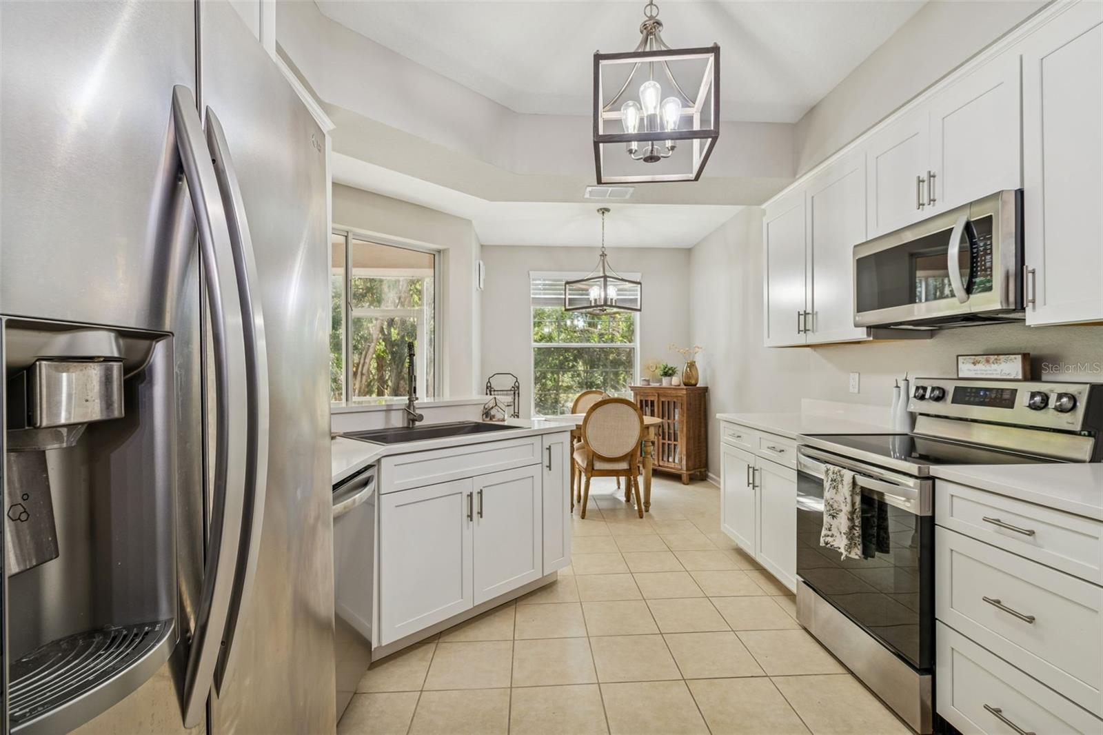 This sleek kitchen features white shaker cabinetry, stainless appliances, quartz countertops, and a tile floor.
