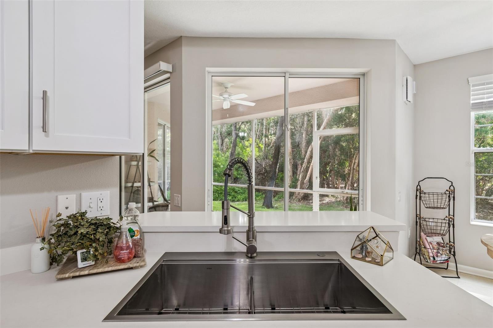 Spacious undermount stainless sink with pull-down sprayer faucet overlooks the screened lanai and lush greenery beyond.