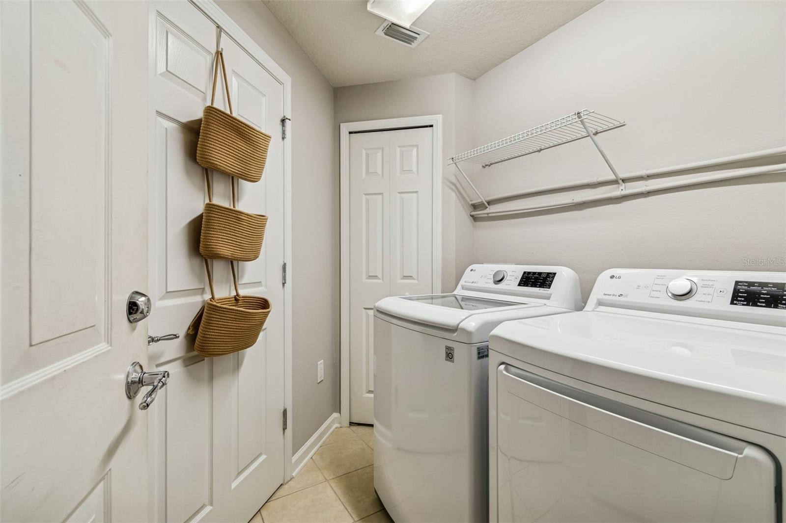 A functional laundry space with full-size LG washer and dryer, overhead shelving, and convenient storage closet.
