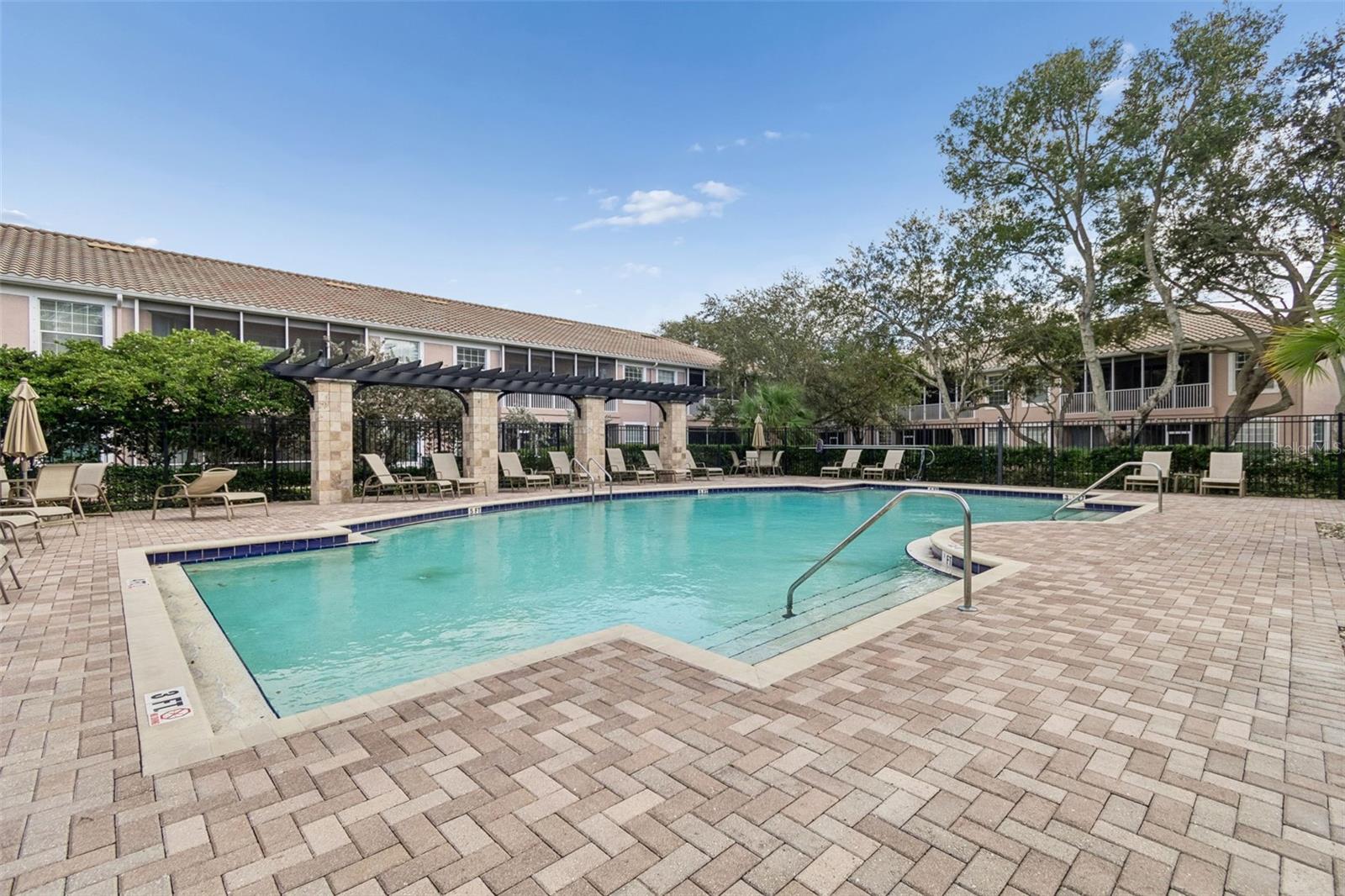Relax beneath sunny Florida skies by this sparkling pool, surrounded by elegant stone pavers, shaded pergolas, and ample lounge seating – the ideal spot to unwind and enjoy a luxurious day outdoors.