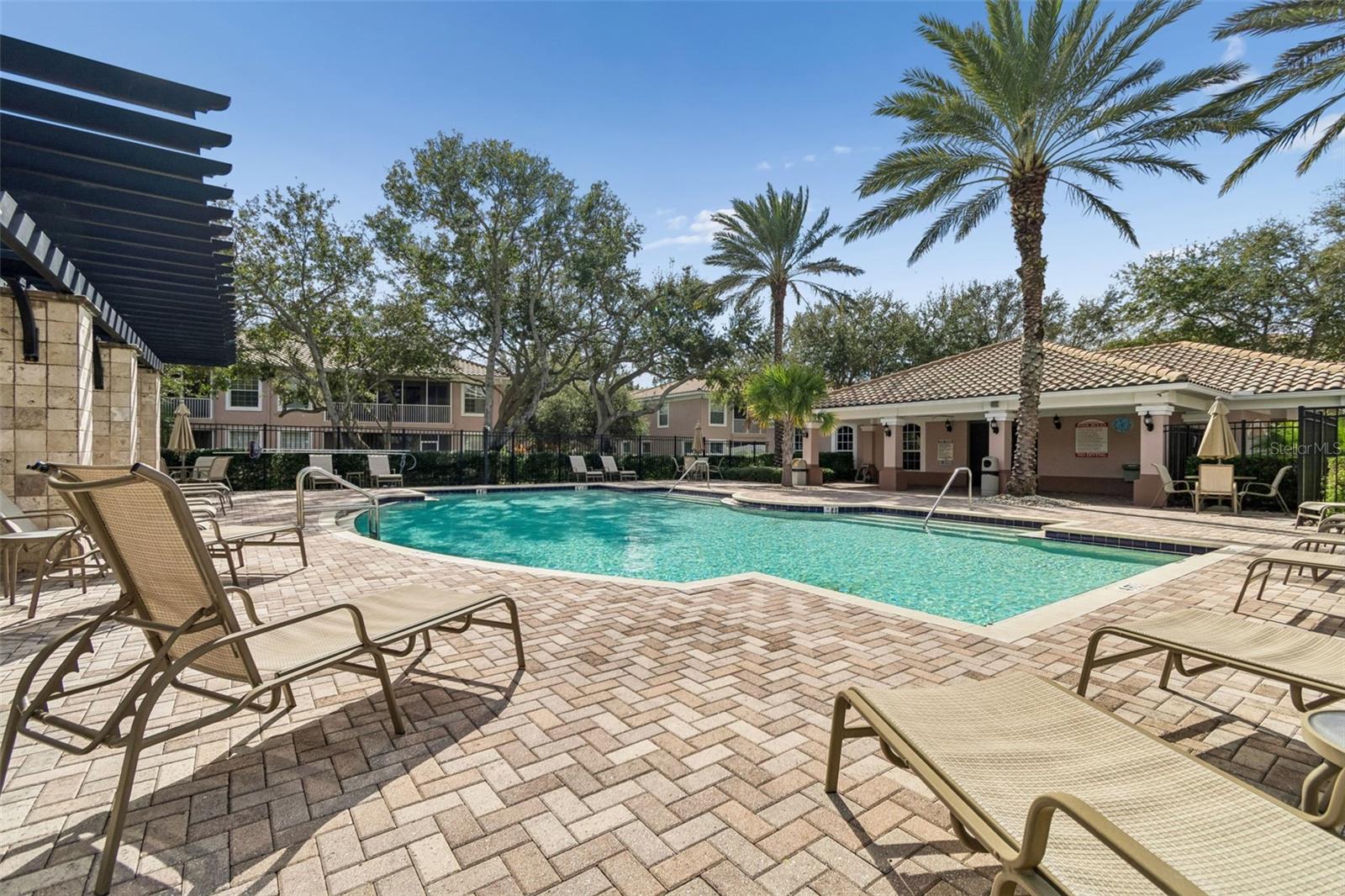 This serene, resort-like pool area is lined with chaise lounges and enhanced by mature landscaping and a stylish clubhouse backdrop, delivering a picture-perfect escape right at home.