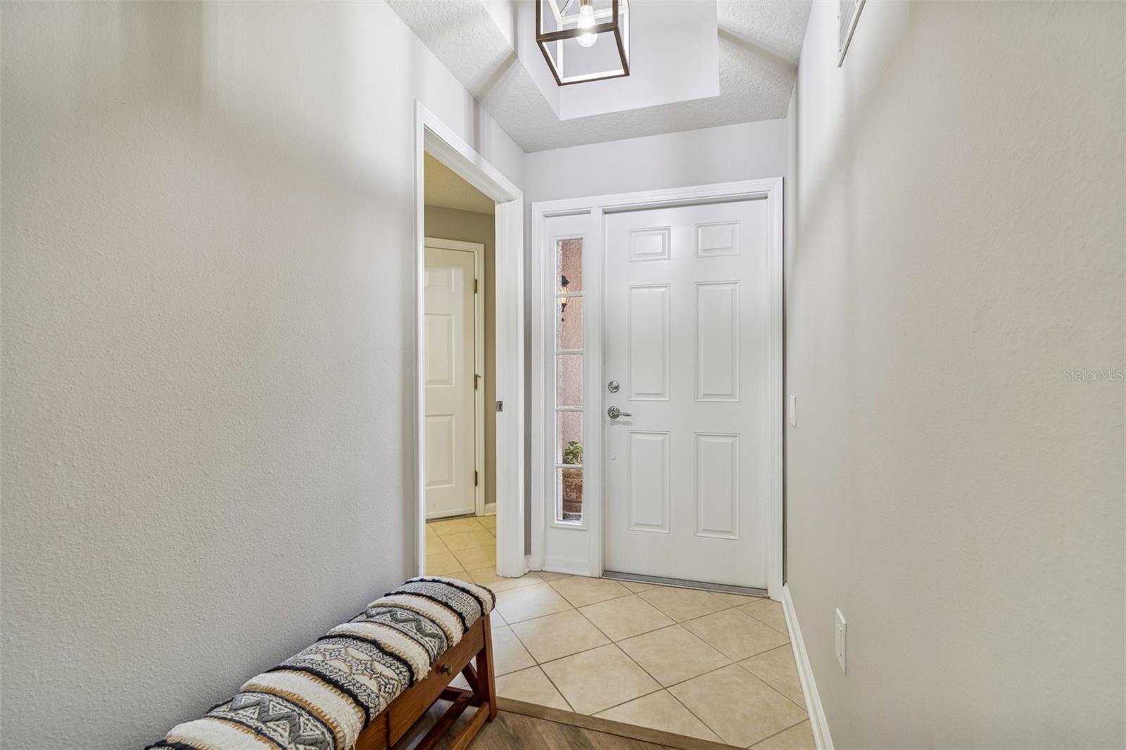 Tile flooring meets laminate in this welcoming interior entrance, accented by a statement light fixture and natural light from sidelights.