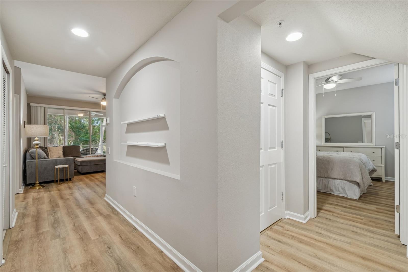 The main hall leads to the living space and bedrooms, featuring built-in display niches and sleek wood-look floors.