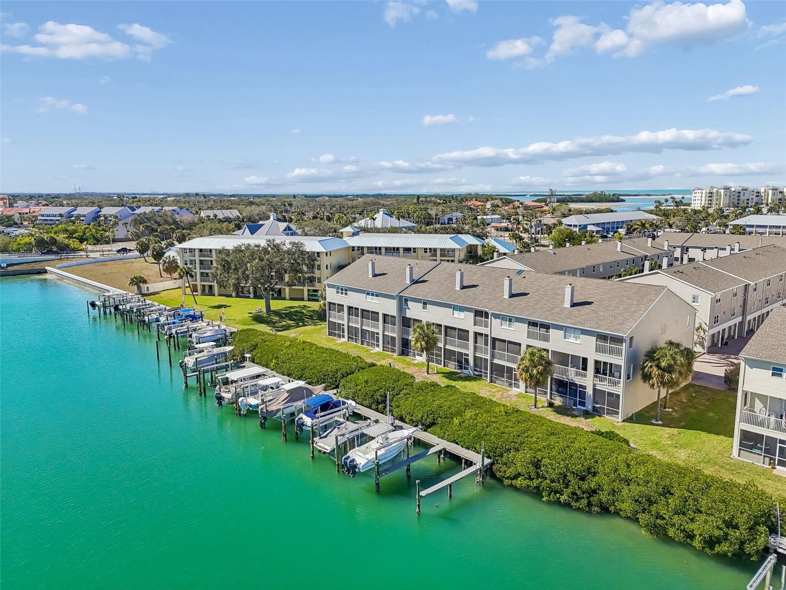Aerial waterfront view showcasing private boat slips, deep-water canal access, and a well-maintained coastal community with lush green surroundings and open water nearby.