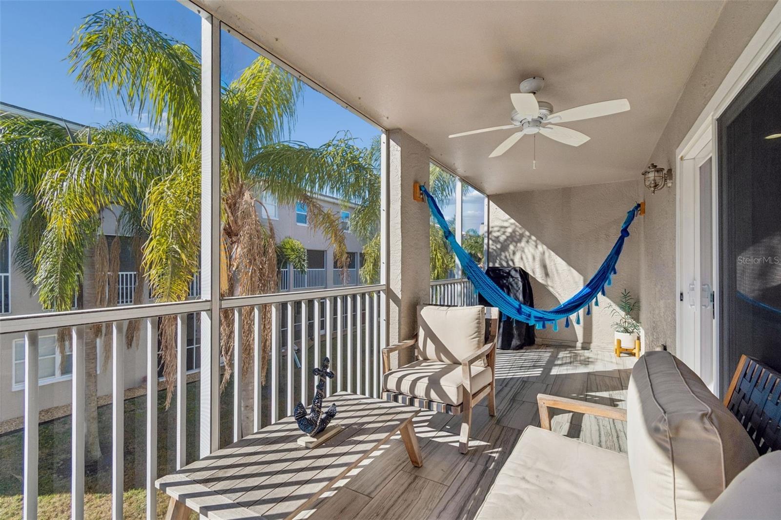 Screened, covered balcony with a relaxing hammock and comfortable seating, offering peek-a-boo water views and a breezy coastal atmosphere.