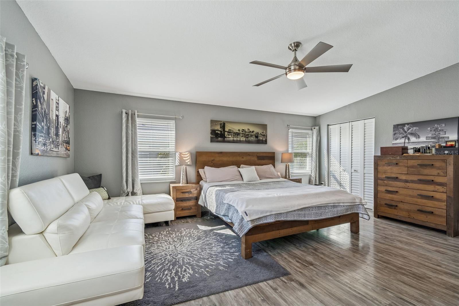 Large main bedroom with wood floors, modern ceiling fan, natural light, sitting area, and three closets for ample storage.