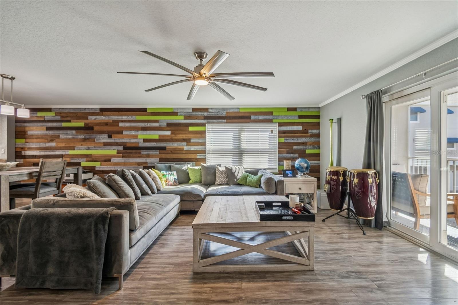 Bright open living area with engineered hardwood floors, a custom shiplap accent wall, and large sliding doors that fill the space with natural light and lead to a private balcony.