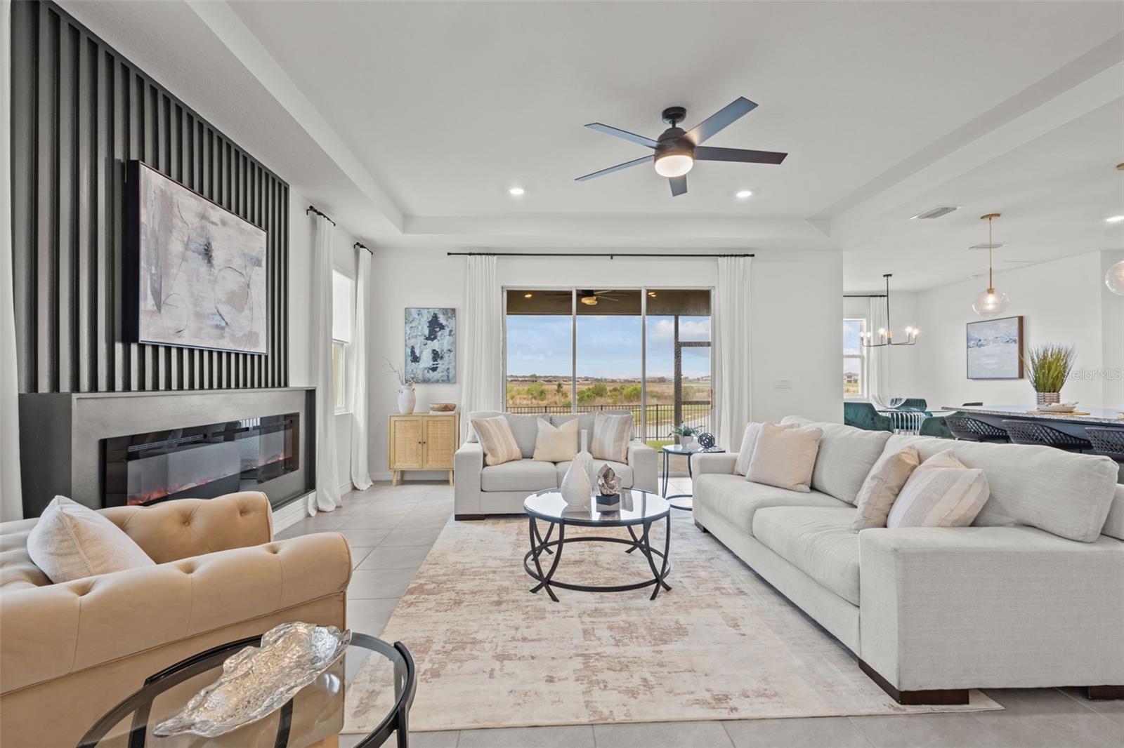 Light-filled great room with wood-look tile floors and a wall of stacking glass sliders that open completely to the covered lanai and pond views.