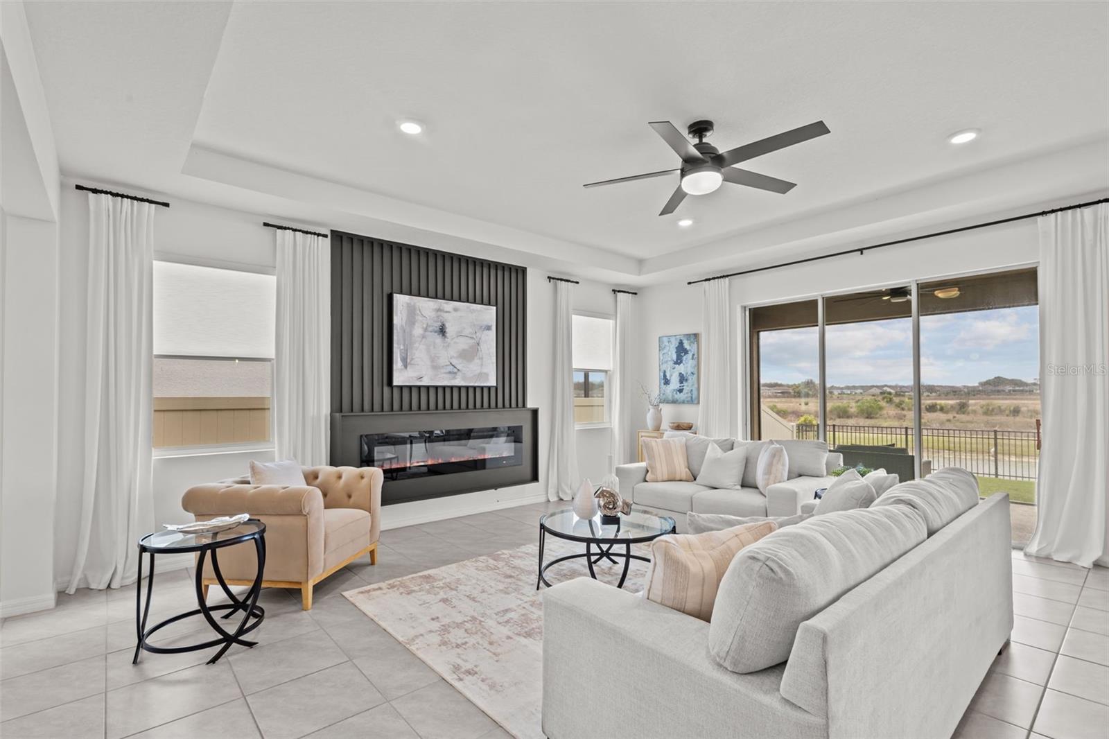 Light-filled great room with wood-look tile floors and a wall of stacking glass sliders that open completely to the covered lanai and pond views.