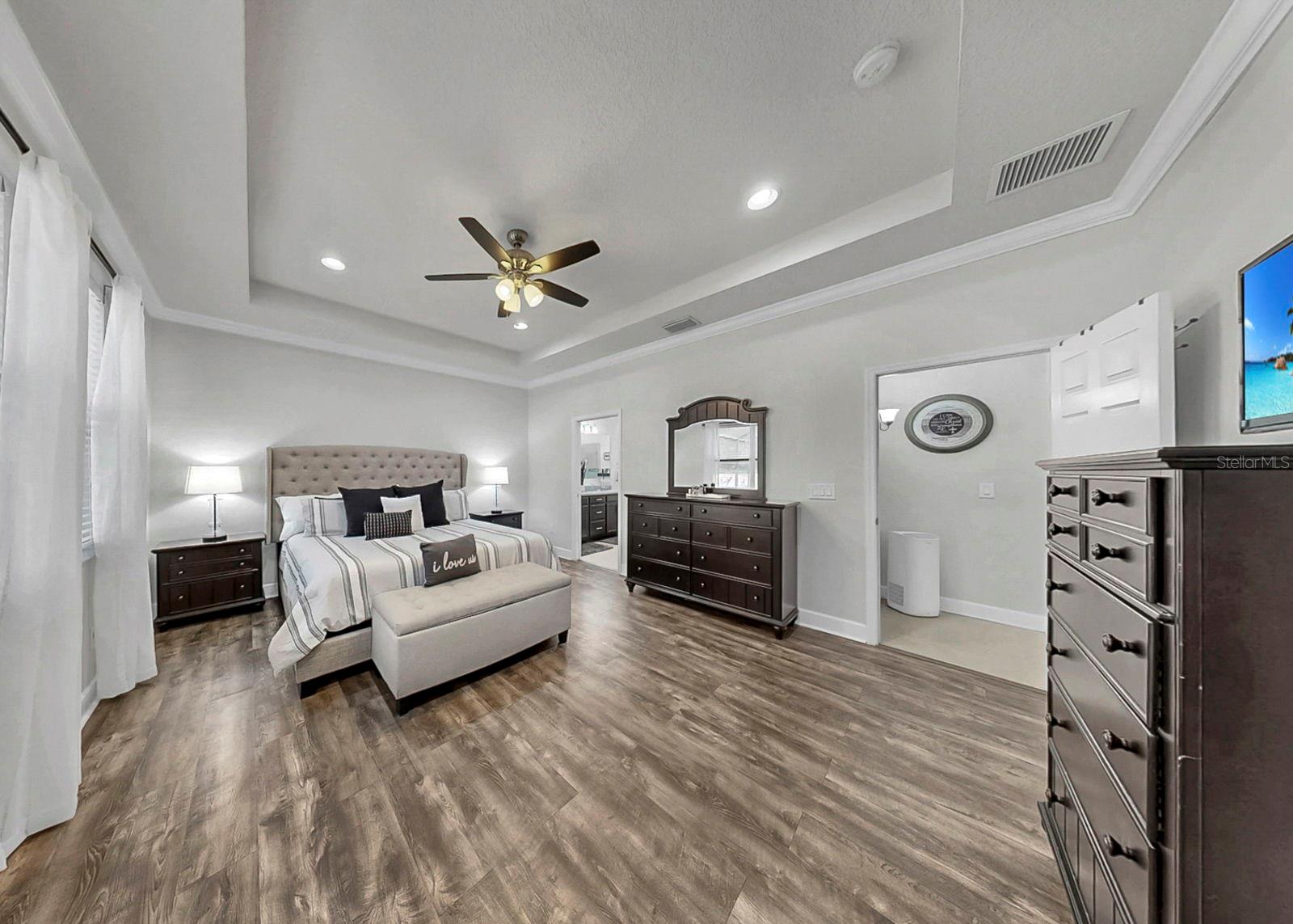 Downstairs primary bedroom with tray ceilings and luxury vinyl flooring