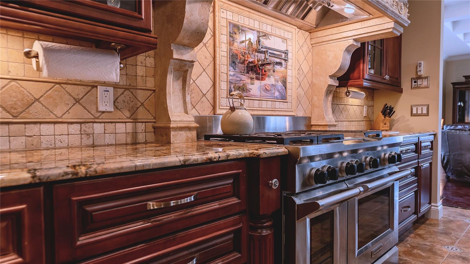 Where culinary artistry meets craftsmanship — a statement gas range framed by custom stonework, rich wood cabinetry, and timeless detail.