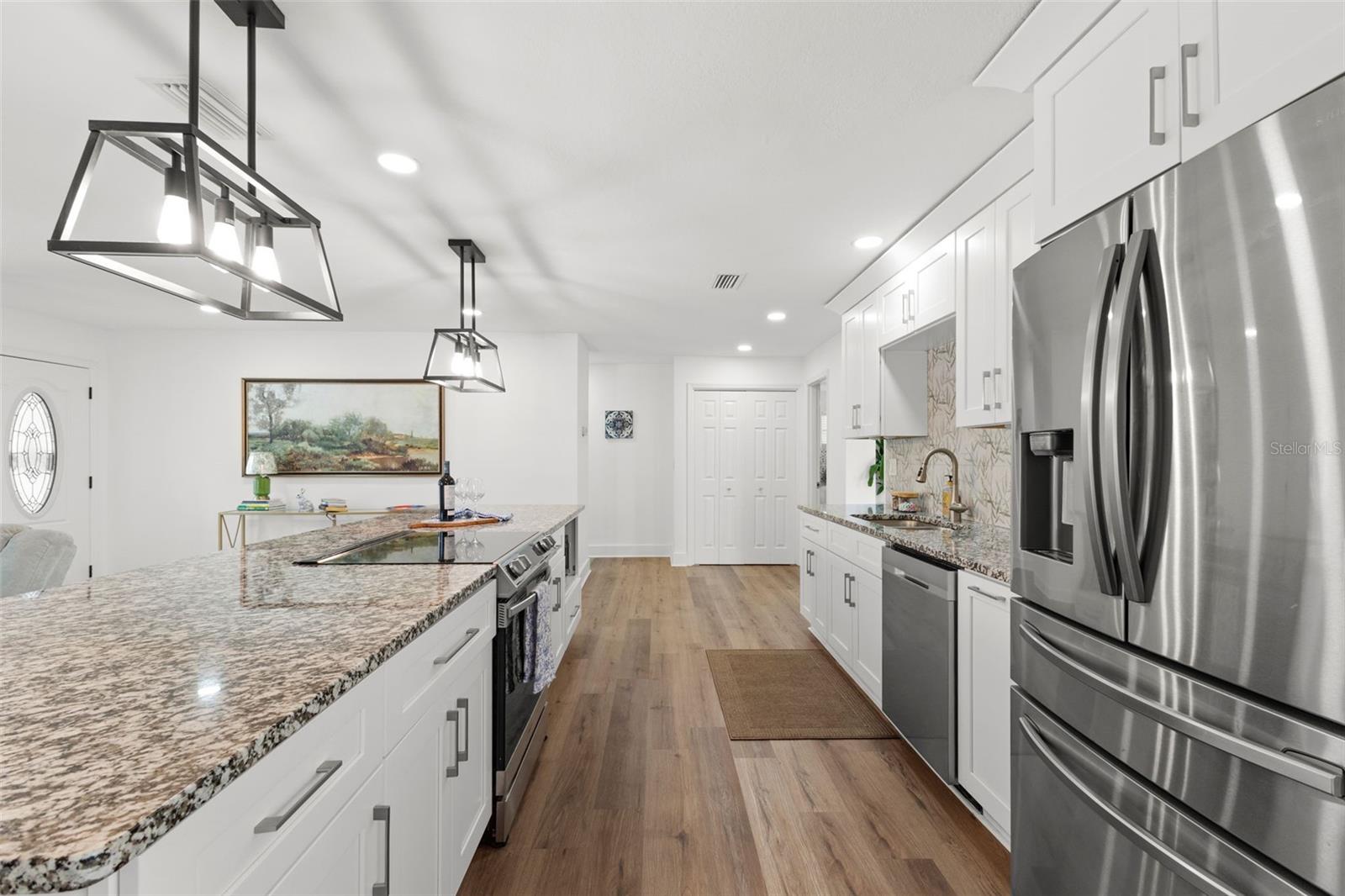 Large center island featuring granite countertops and built-in storage, including integrated microwave space for convenience. Stainless steel range is centrally positioned for functional workflow. Open sightlines connect the kitchen seamlessly to the living area and front entry, reinforcing the home’s open-concept design. Upgraded 5-inch baseboards and six-panel doors continue throughout for a cohesive finish.