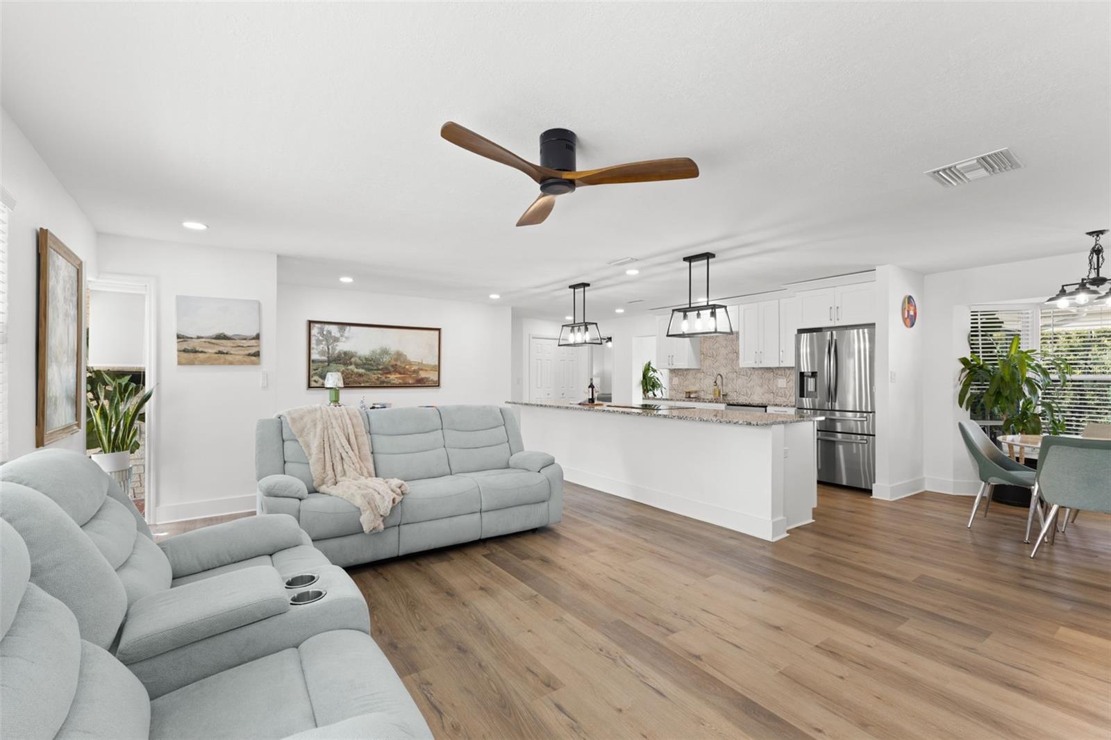 Expansive open-concept layout seamlessly connecting the living room, kitchen, and dining area, enhanced by continuous luxury vinyl plank (LVP) flooring throughout. Recessed lighting and a modern ceiling fan provide both style and comfort.