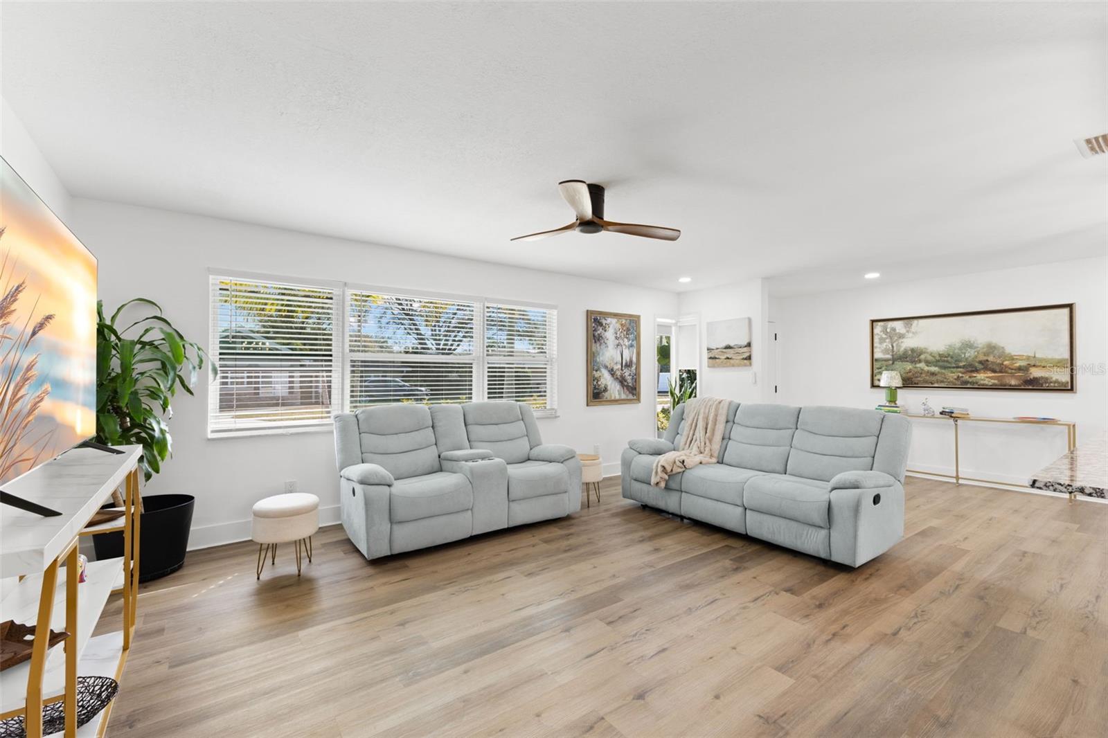 Bright and open living area featuring durable luxury vinyl plank (LVP) flooring throughout, offering both style and low-maintenance performance. Neutral walls enhance the natural light streaming through multiple front-facing windows with white trim and blinds.