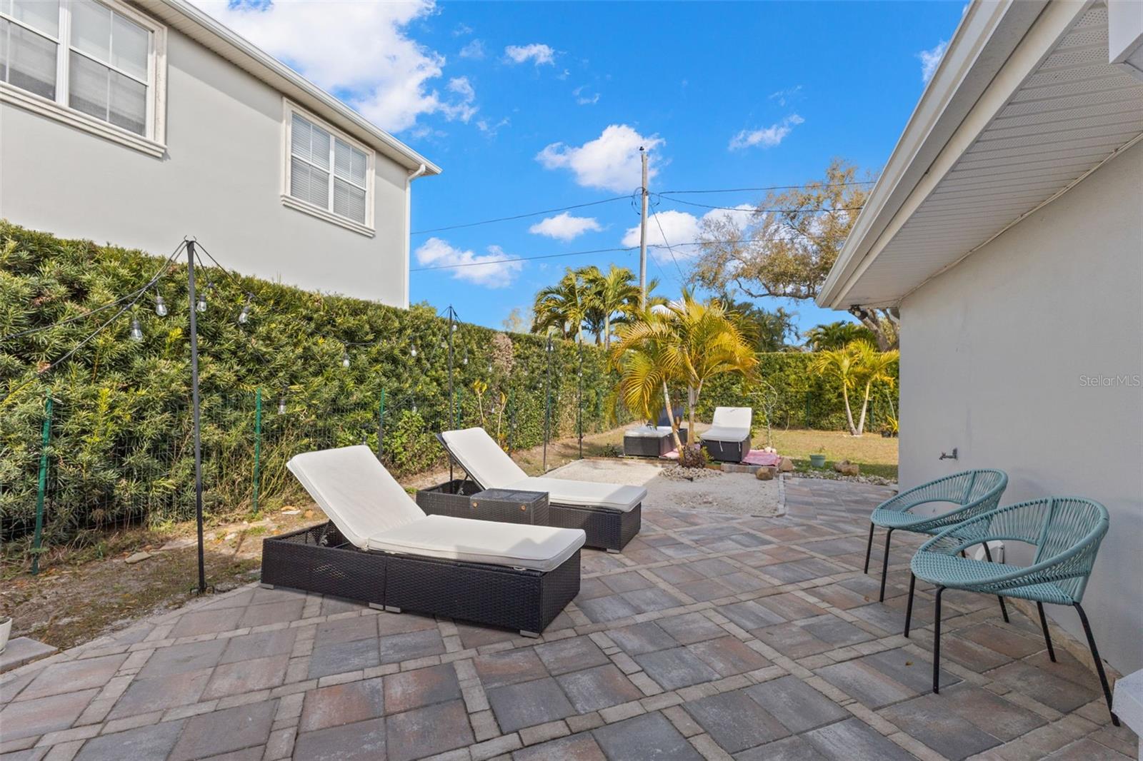 Private backyard retreat featuring an extended paver patio directly off the sunroom, creating seamless indoor-outdoor flow. The spacious hardscaped area offers ample room for seating, dining, or lounging. Mature hedges provide natural privacy along the perimeter, while tropical landscaping enhances the relaxed, coastal setting. The combination of patio and open yard space allows for flexible outdoor use.