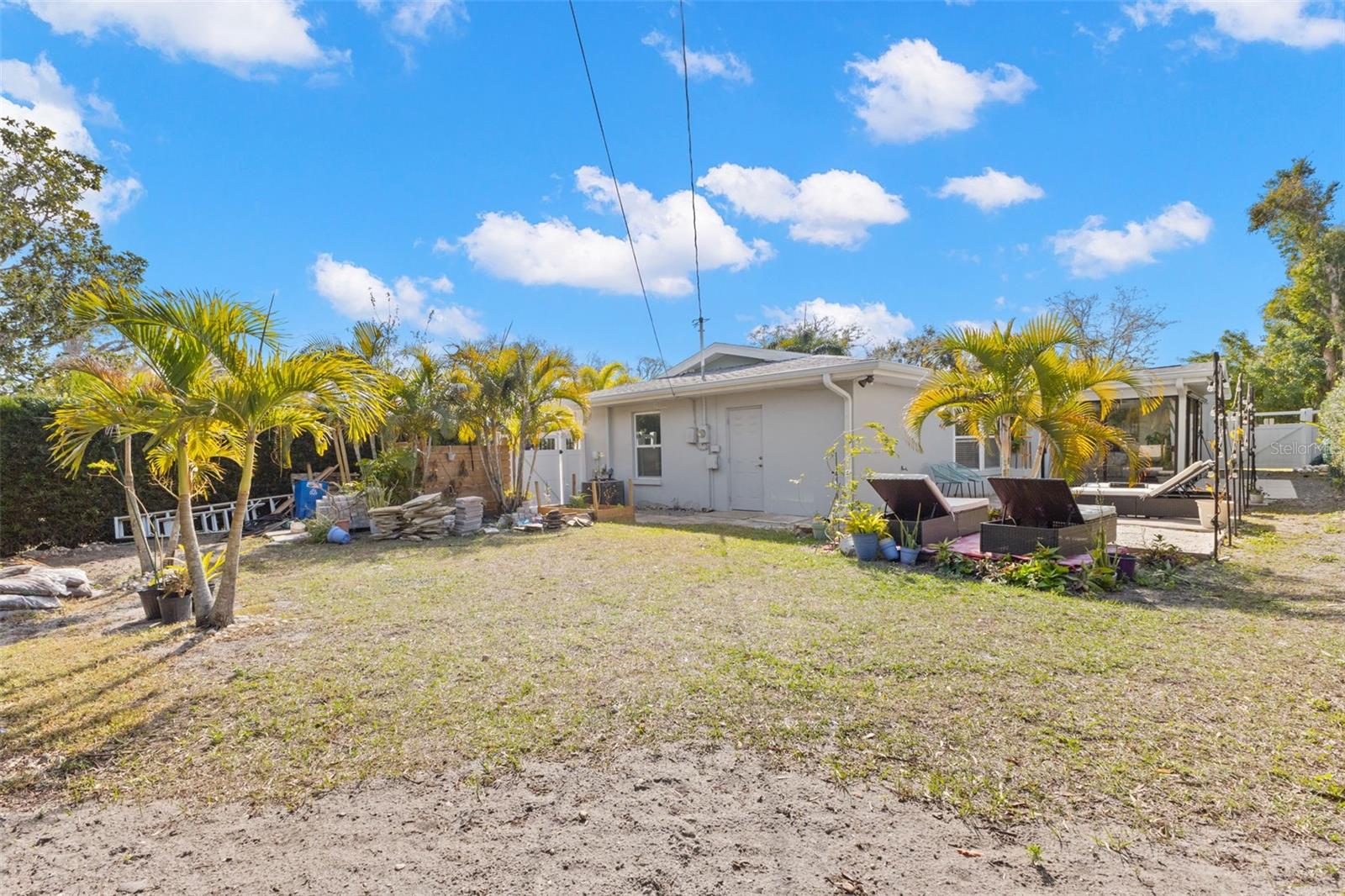 Alternate view of the backyard highlighting the generous yard space and paved patio area, perfect for gatherings, grilling, or future customization. Multiple lounging areas are thoughtfully positioned to enjoy the sunshine.