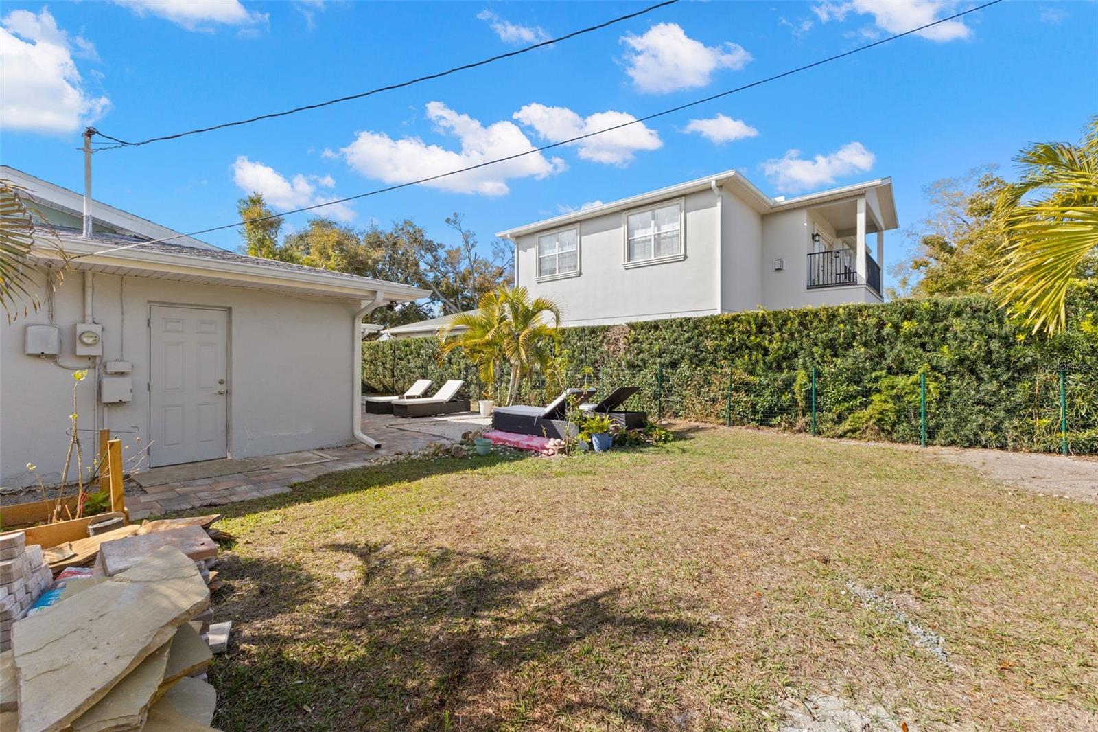 Expansive grassy yard bordered by tall privacy hedges and palm trees, offering room to garden, play, or design your own outdoor retreat. The fully enclosed setting provides a private and peaceful backdrop.
