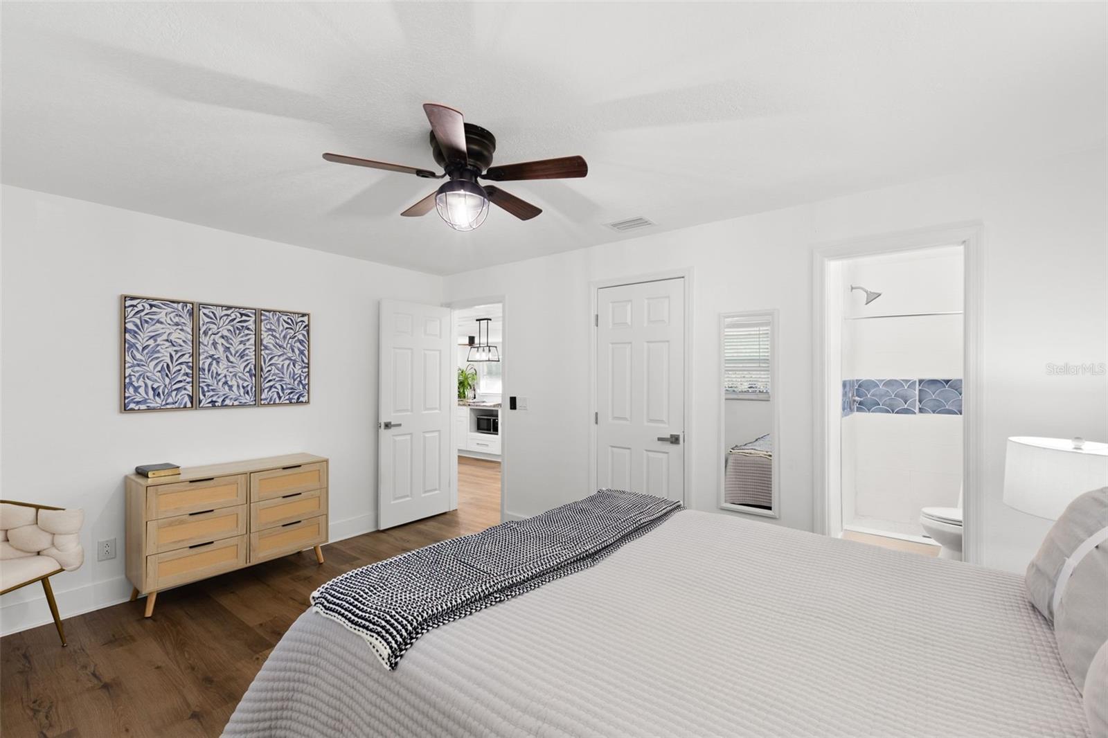 Spacious primary bedroom featuring wood-look LVP flooring, crisp white walls, and a modern ceiling fan with integrated light. The room offers direct access to the ensuite bath and closet area, creating a functional and private retreat. Clean lines and neutral finishes provide a versatile backdrop for any design style.