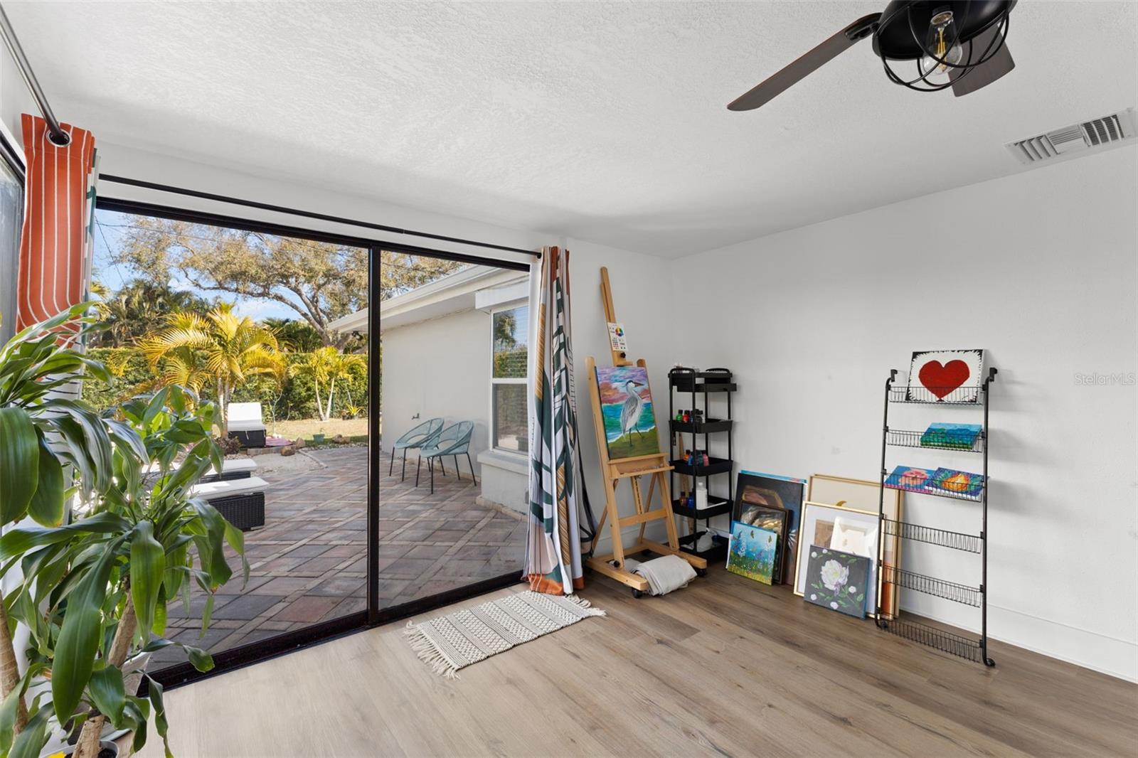 Sun-filled flex space with full-width glass sliders showcasing the landscaped backyard and patio lounge area. Ideal as a home office, studio, or additional living area, the room offers generous wall space and open floor area for versatile use. Neutral finishes enhance the light, open feel.