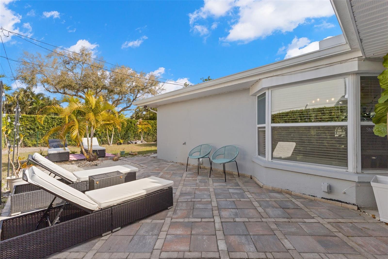 Extended paver patio runs along the rear elevation, bordered by low-maintenance landscaping and decorative stone accents.