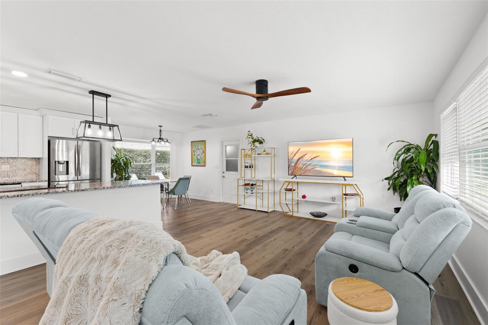 Wide, open-concept main living area showcasing continuous luxury vinyl plank (LVP) flooring and a seamless flow between living, kitchen, and dining spaces. Recessed lighting and a modern ceiling fan provide both illumination and comfort, while upgraded 5-inch baseboards add a refined architectural finish.