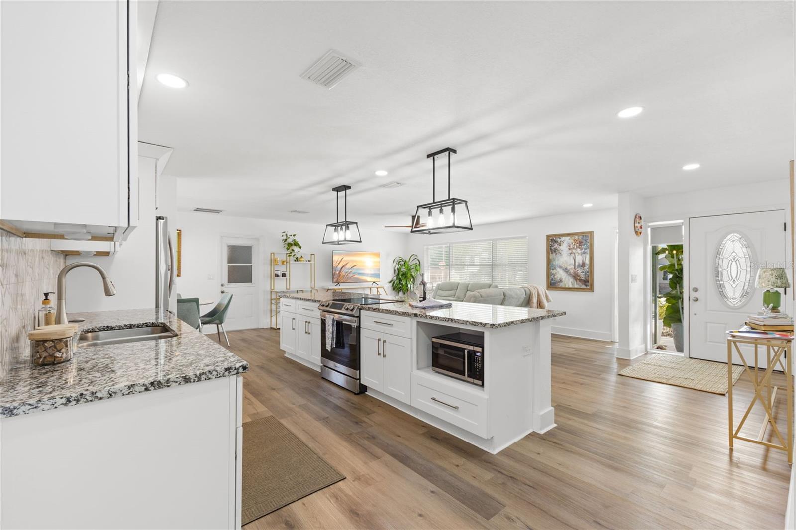 Spacious kitchen corridor with uninterrupted LVP flooring and recessed lighting for a bright, streamlined look. Granite-topped island houses the cooktop/range area, creating a practical work triangle. Extended cabinetry and counter space offer ample storage and prep areas. Clean white finishes and modern hardware deliver a timeless, move-in-ready presentation.