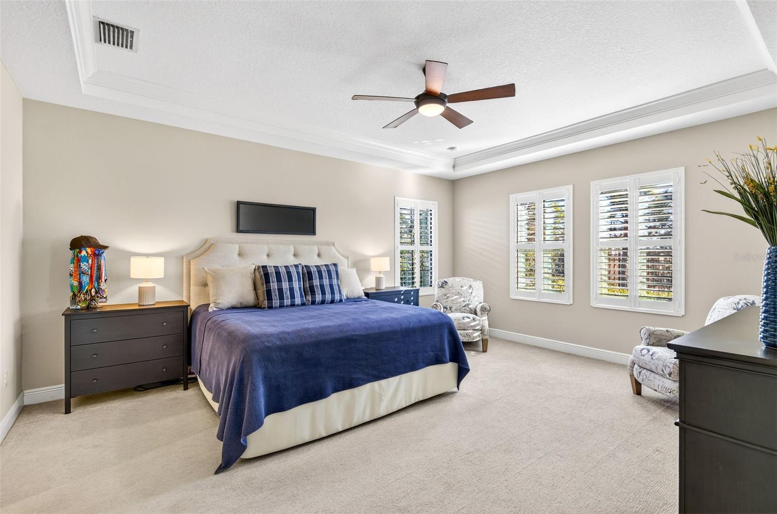 Primary bedroom with plantation shutters, ceiling fan and a view of the backyard oasis