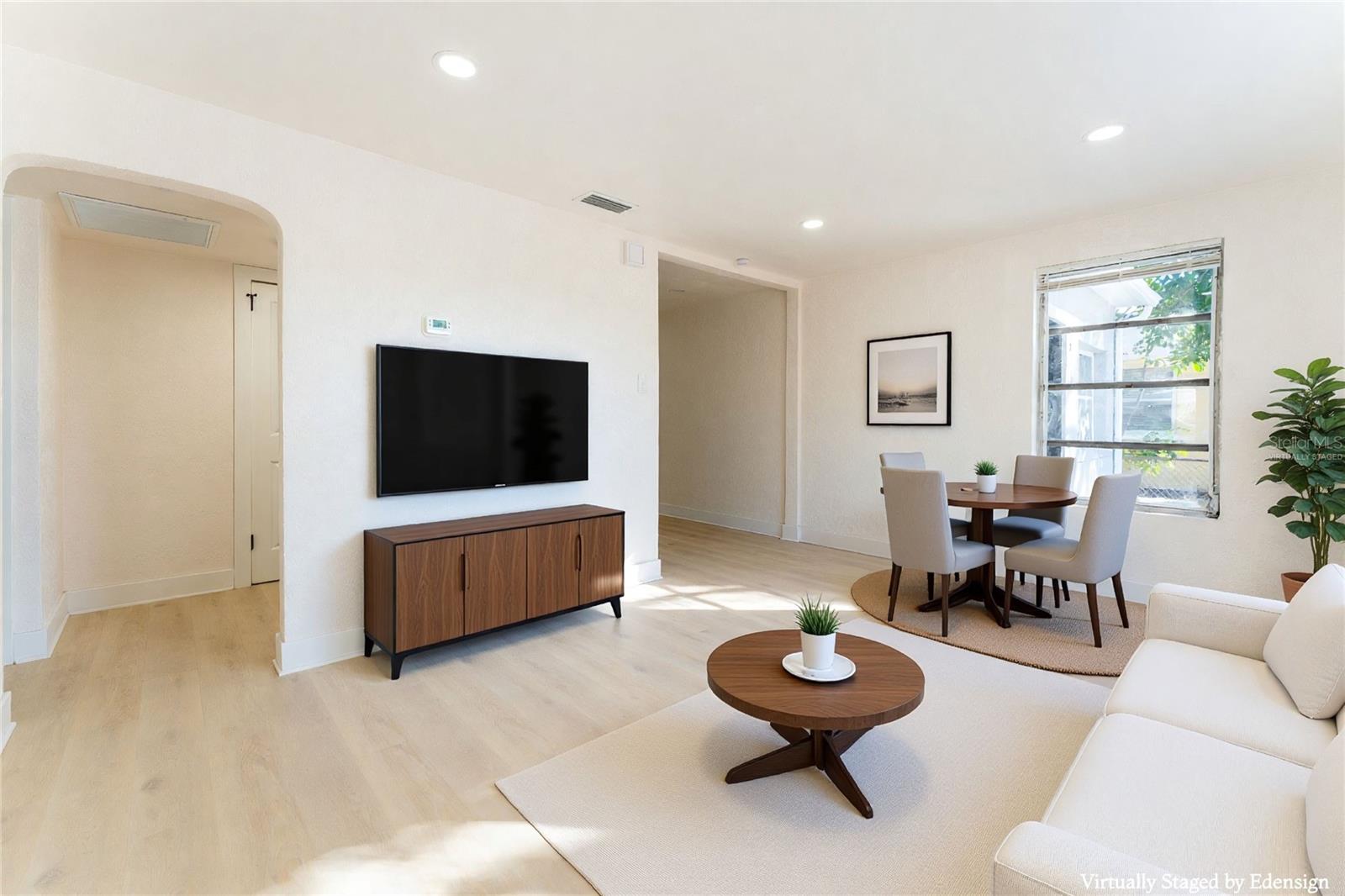 Light-filled great room just off the front entry featuring an open-concept layout with seamless flow into the dining area and kitchen. Large windows bring in natural light, highlighting the updated flooring and clean, modern finishes throughout. The layout offers flexibility for both everyday living and entertaining. Furniture has been virtually staged to illustrate scale and layout possibilities.