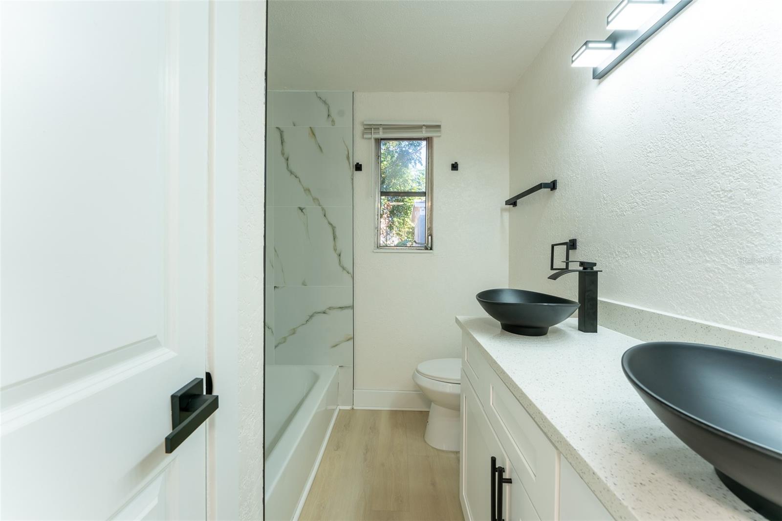 Fully updated bathroom featuring a modern double vanity with sleek vessel sinks, contemporary matte black fixtures, and ample counter space. The shower/tub combo is accented with stylish tile, while updated lighting and finishes create a clean, elevated look throughout.