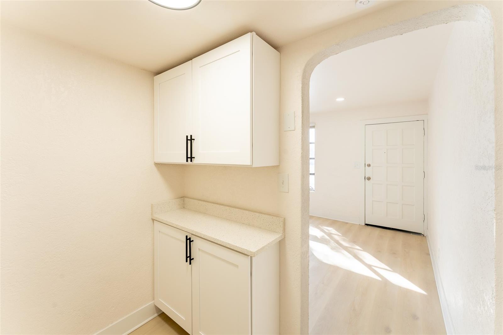 Convenient utility area located just off the living room, offering additional cabinet storage and countertop space. Perfect for a coffee station, linen storage, or everyday organization before entering the bathroom and bedroom area.