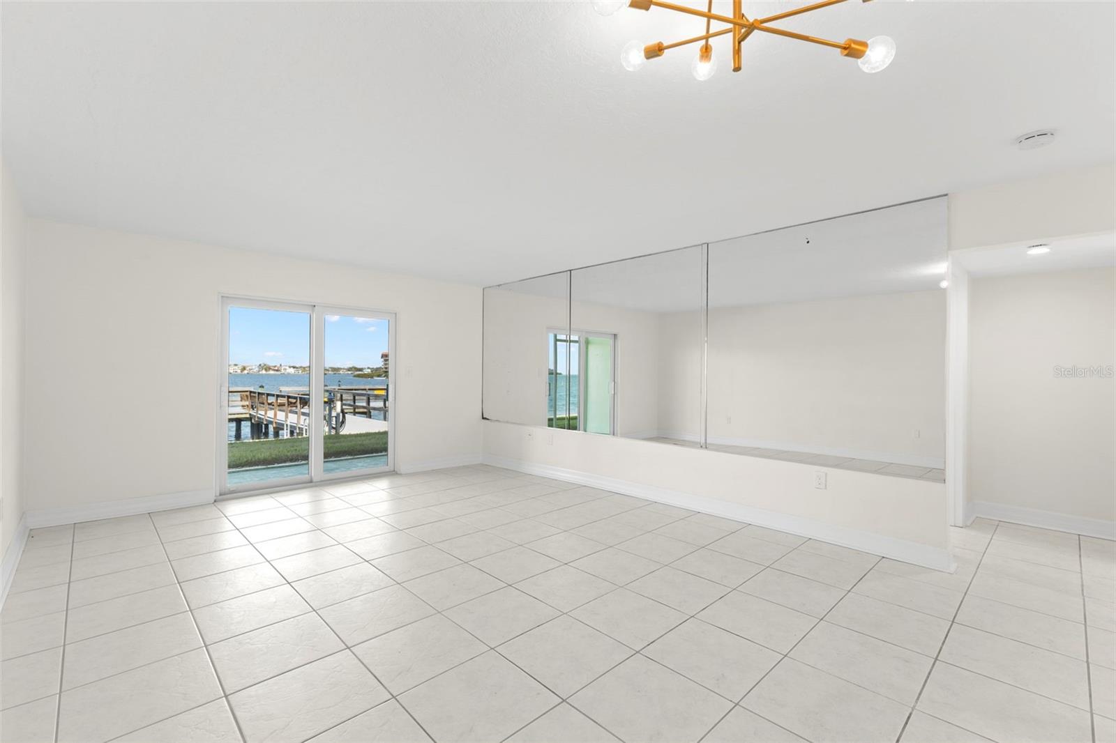 The living room is filled with natural light and enhanced by a full mirrored accent wall, while sliding glass doors showcase tranquil Intracoastal views and seamless indoor-outdoor flow.