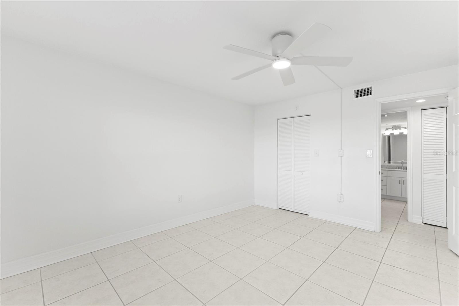 Primary bedroom with 18 X 18 ceramic tile flooring, ceiling fan, double-door closet, and direct access to the bathroom.