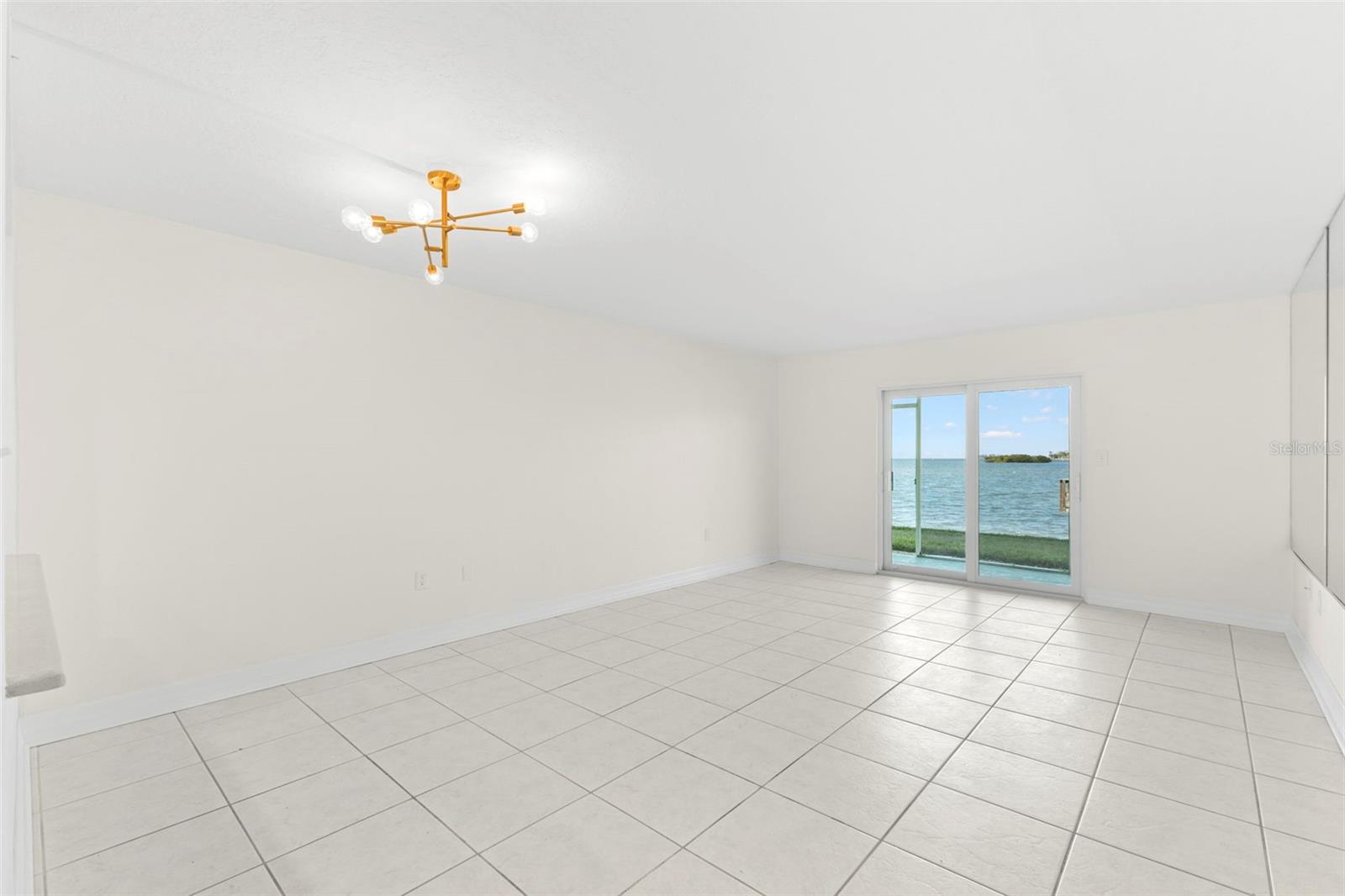Expansive dining/living room with 18 X 18 neutral ceramic tile flooring and sliding glass doors framing sweeping water views just steps from the shoreline.