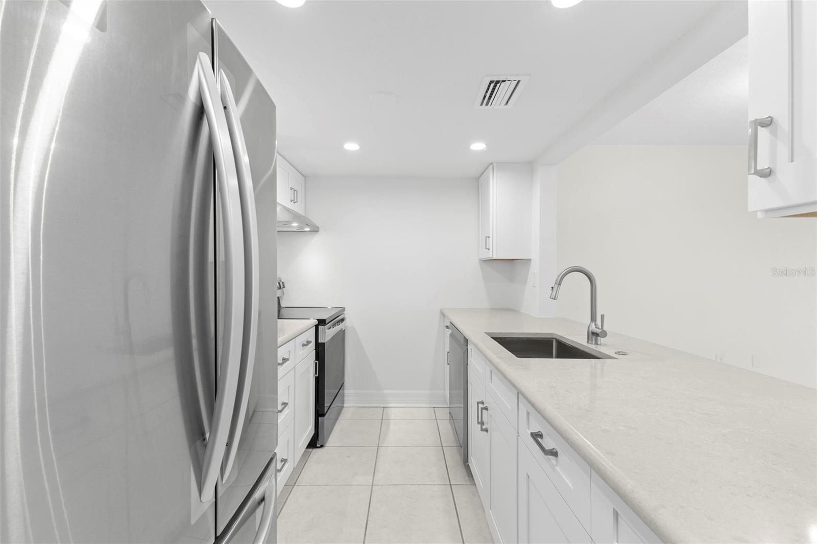 Efficient galley kitchen offering generous Corian countertop space, integrated sink with gooseneck faucet, stainless appliances, and ample cabinetry.